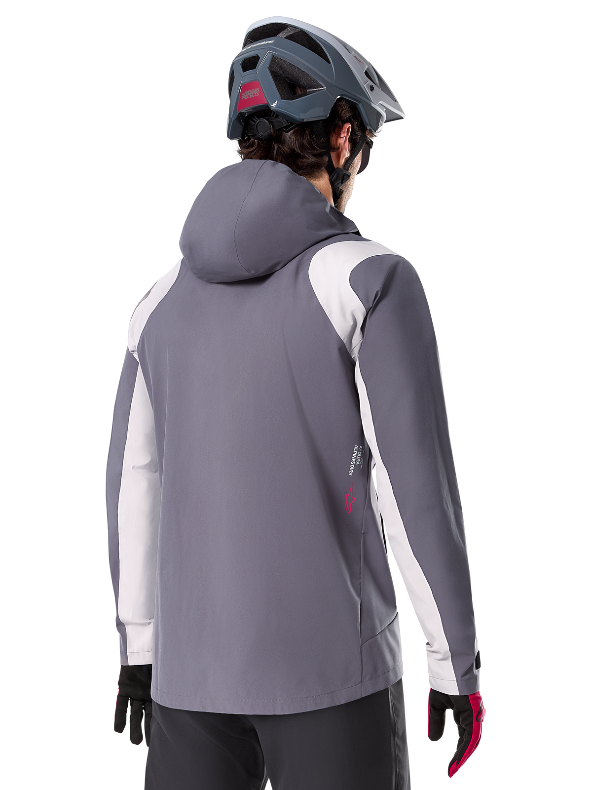 Chaqueta impermeable Alpinestars A-Dura, chaqueta de mountain bike, gris titanio oscuro, vista trasera con paneles en gris claro en hombros y brazos, detalle de logotipo rojo en el lateral, usada con casco de MTB gris y guantes negros y rojos, ropa técnica para ciclismo de montaña