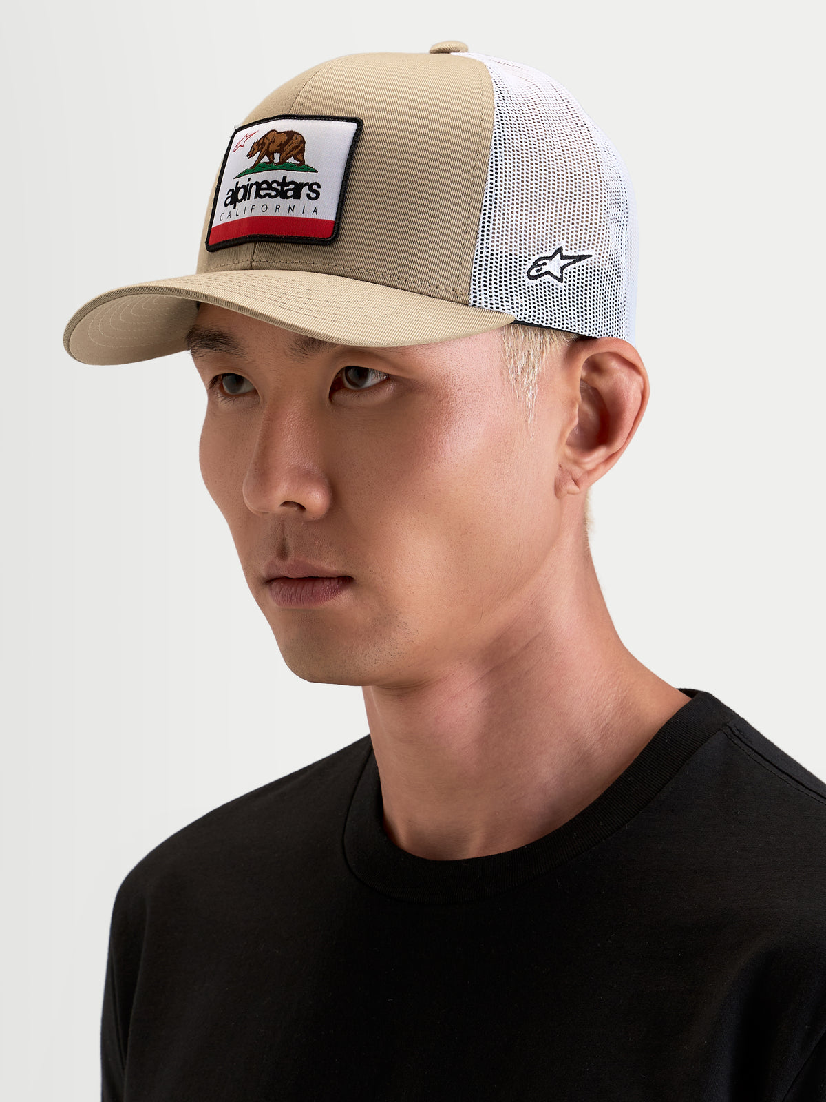 Alpinestars Cali 2.0 Gorra, gorra sportswear estilo trucker en caqui y blanco, vista en modelo, con visera curva, corona estructurada de sarga, malla trasera transpirable y parche tejido de California