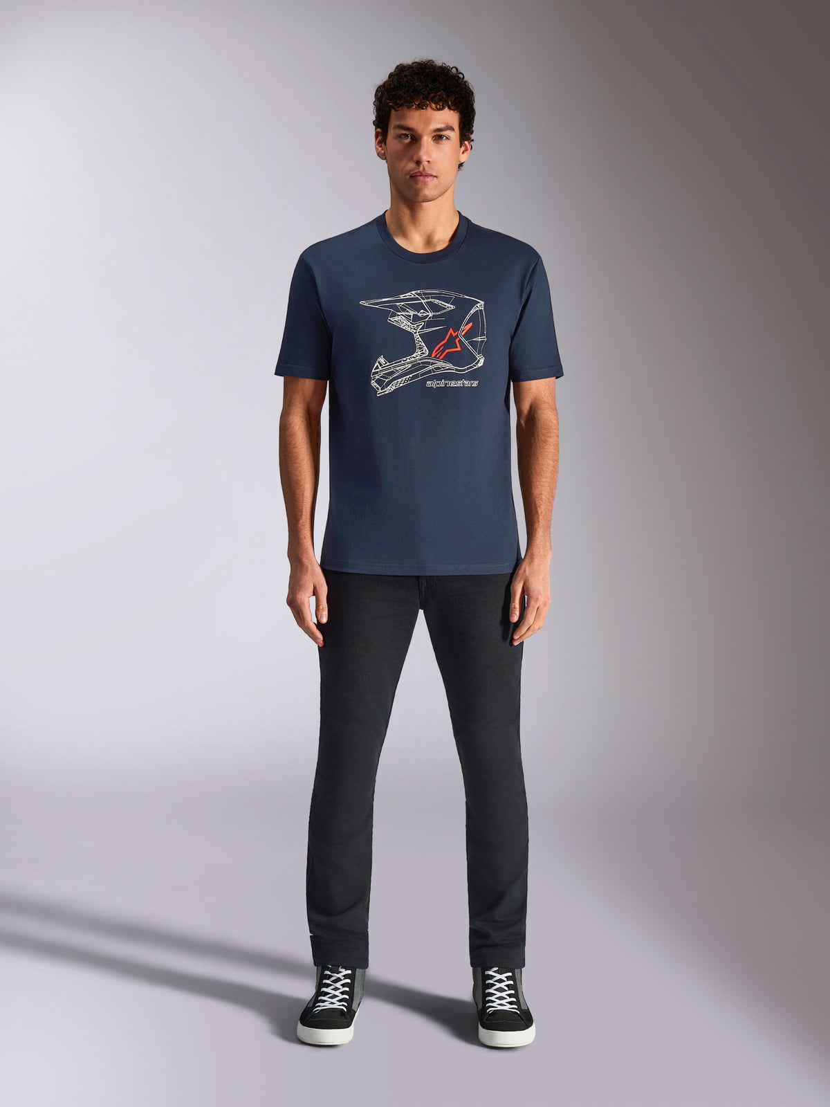 Camiseta Alpinestars MX Helmet CSF, camiseta de manga corta, azul marino, con un gráfico de casco de motocross blanco y el logo de la estrella roja, usada por un modelo con pantalones negros y zapatillas, ropa urbana casual inspirada en el motociclismo