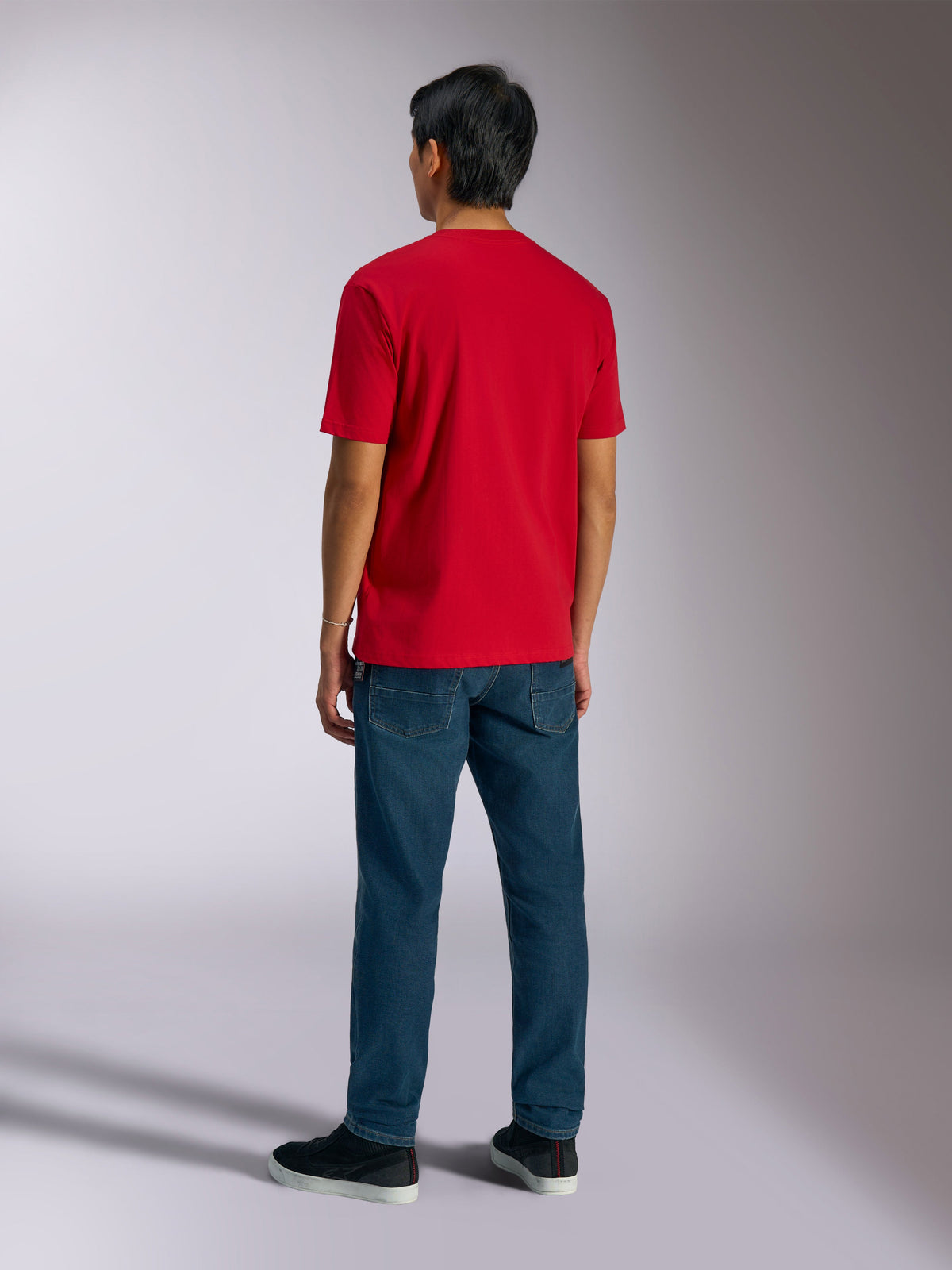 Alpinestars Ageless Shadow CSF Tee, camiseta de manga corta roja, vista posterior de un modelo con vaqueros azules y zapatillas negras, estilo casual motorsport streetwear