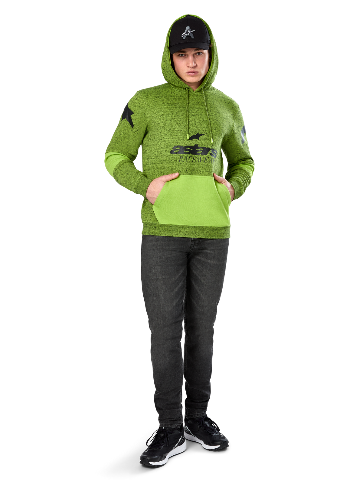 Alpinestars Perpetuate Hoodie, sudadera de forro polar jaspeado verde lima con bolsillo canguro y paneles en las mangas en verde brillante a contraste, gráfico frontal 'astars' en negro, combinada con gorra negra y vaqueros oscuros, ropa urbana casual inspirada en el motorsport
