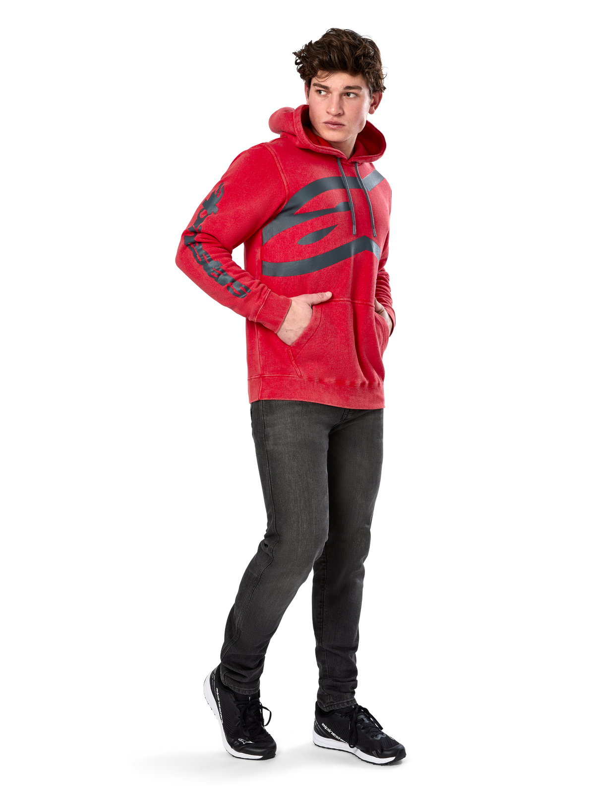 Sudadera con capucha Alpinestars Unbound, forro polar rojo teñido en prenda, logotipo oscuro extragrande en el pecho y marca en las mangas, bolsillo canguro, capucha con cordón, usada por un modelo con vaqueros gris oscuro y zapatillas negras, ropa urbana casual inspirada en el automovilismo
