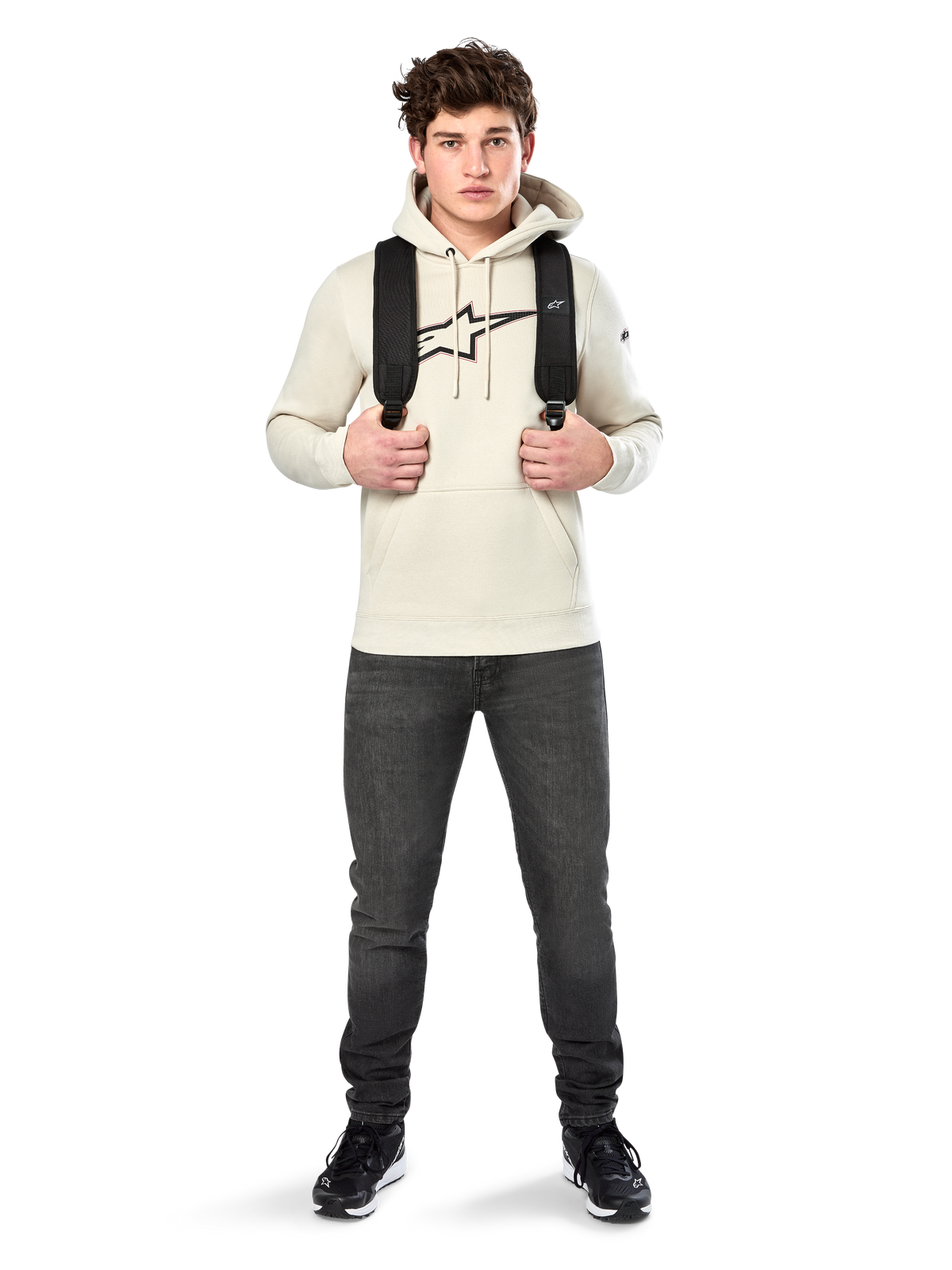 Sudadera con capucha Alpinestars Insignia, ropa urbana casual, sudadera de forro polar Off White, logotipo con apariencia de fibra de carbono y contorno rojo, capucha con cordón, bolsillo canguro, vestida por un modelo con mochila negra y vaqueros gris oscuro