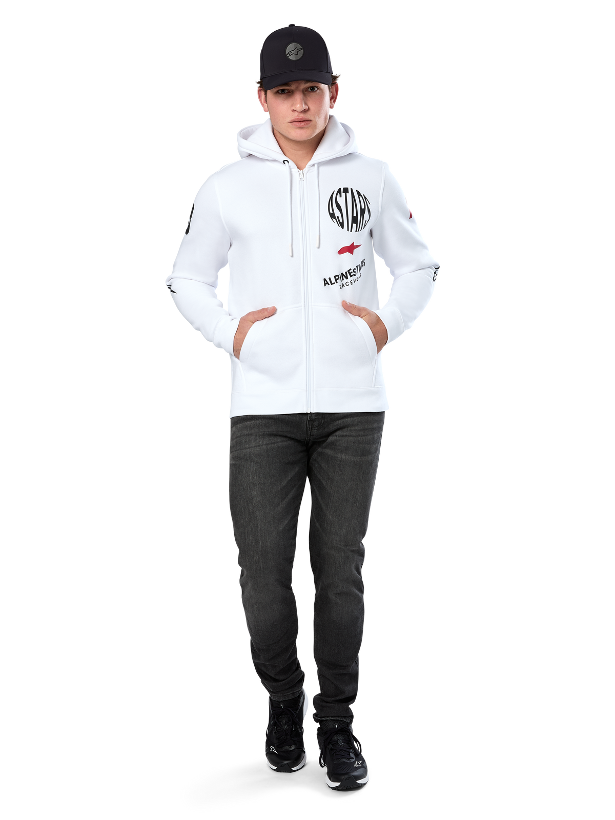 Alpinestars Variegate Hoodie, sudadera blanca de forro polar con cremallera, arte de múltiples logotipos con 'ASTARS' y logotipo de estrella roja en el pecho, detalles gráficos en las mangas, usada por un modelo con gorra negra y vaqueros negros, moda urbana casual de motorsport
