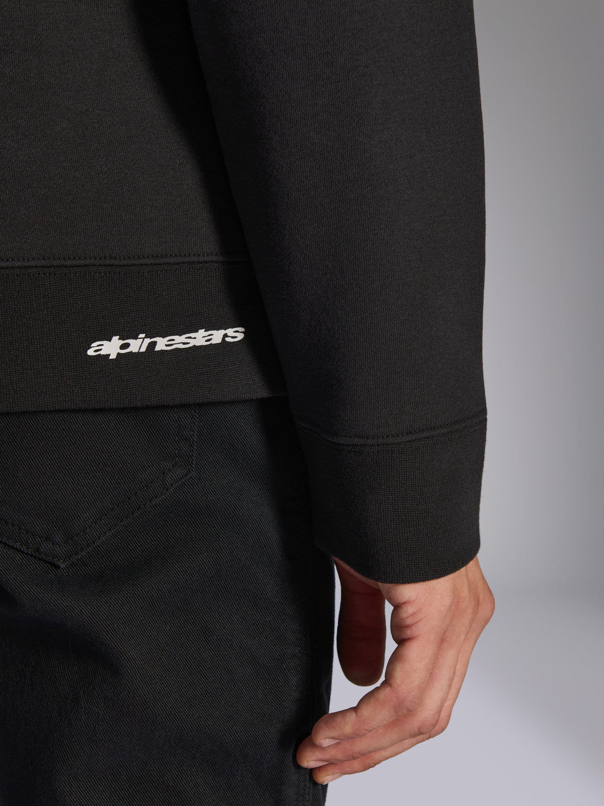 Alpinestars Positive Crew, sudadera negra, detalle de primer plano del dobladillo y puño acanalados con logotipo de Alpinestars en blanco, textura de tejido premium, ropa deportiva casual inspirada en el automovilismo