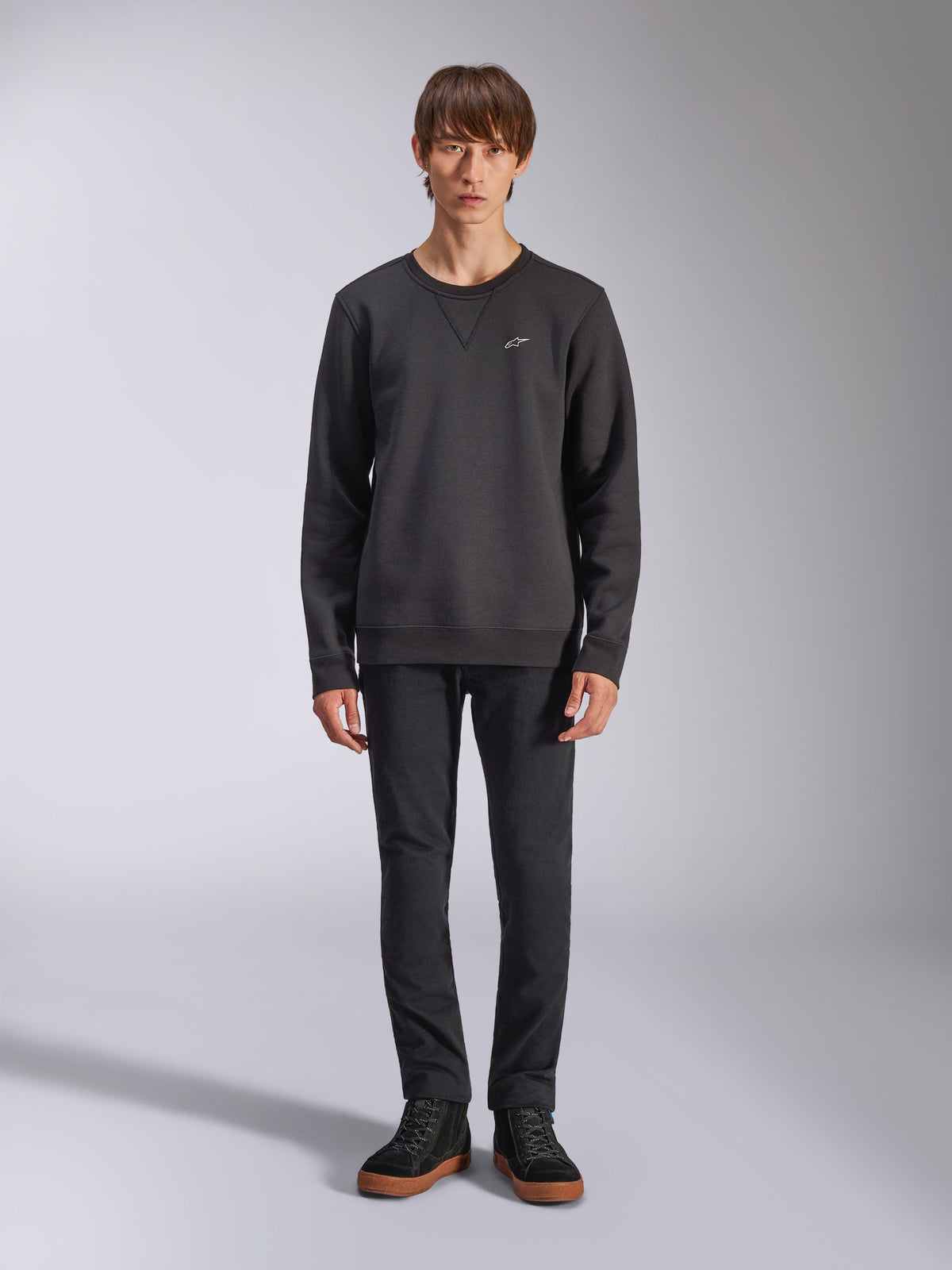 Sudadera Alpinestars Positive Crew, sudadera negra casual de cuello redondo, pequeño logotipo blanco en el pecho, detalle de costura en V en el cuello, foto de estudio de cuerpo completo con modelo vistiendo pantalones negros y zapatillas, ropa de estilo de vida inspirada en el automovilismo