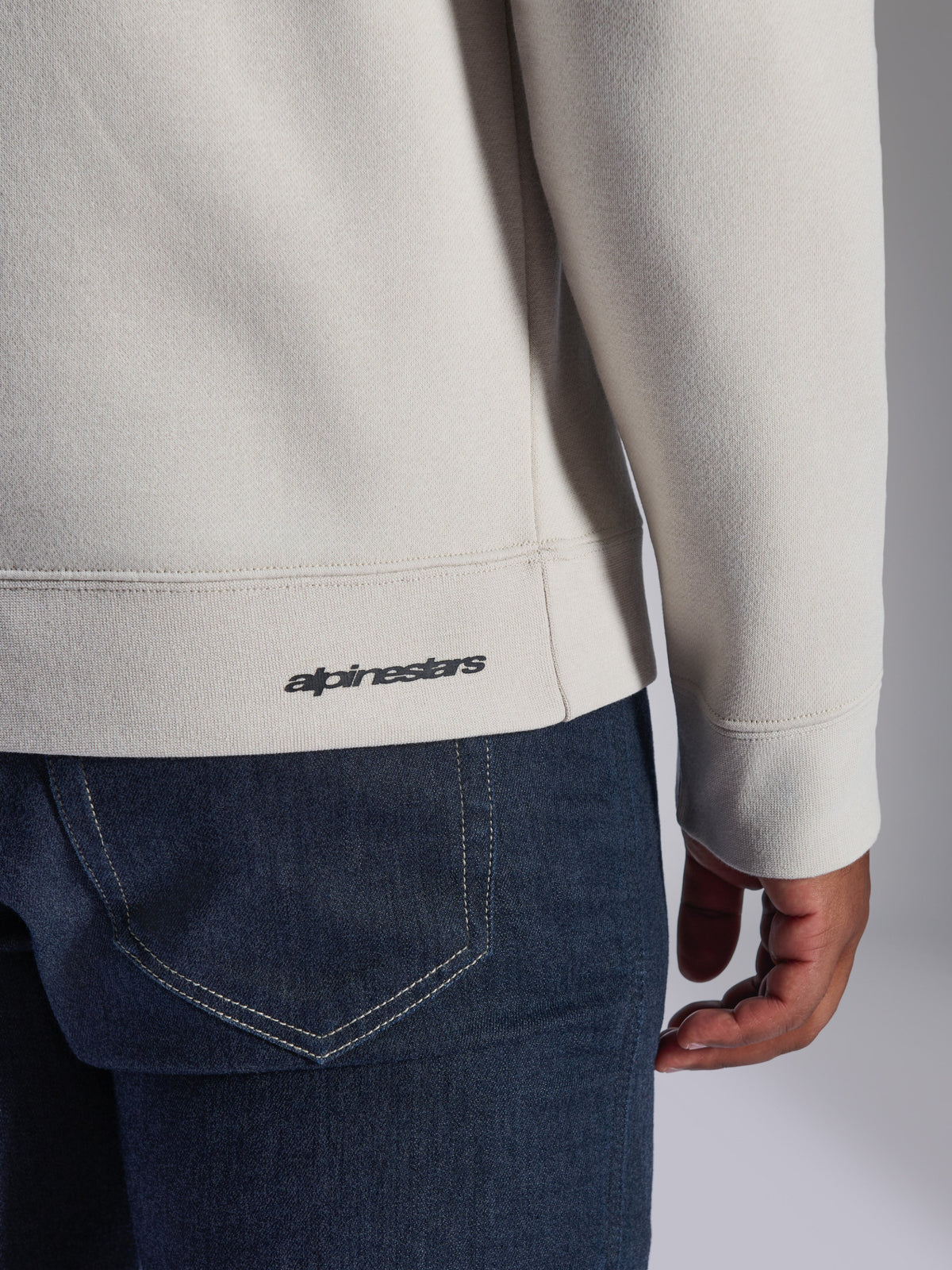 Sudadera Alpinestars Positive Crew, blanco roto, detalle de primer plano del dobladillo y el puño acanalados, con un pequeño logotipo negro de Alpinestars, ropa casual inspirada en el automovilismo