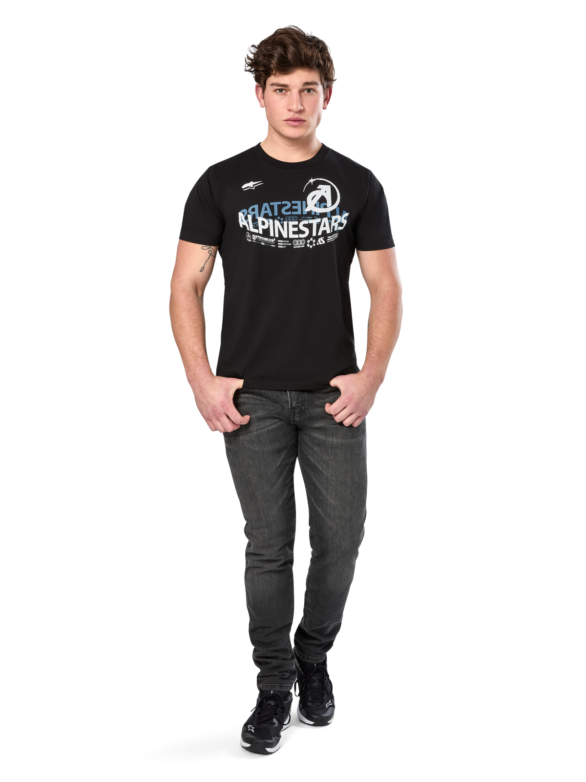 Alpinestars Semicircle CSF Tee, camiseta de manga corta, negra, gráfico curvado en blanco y azul claro en el pecho, usada por un modelo con vaqueros gris oscuro y zapatillas negras, ropa urbana casual de estilo motor