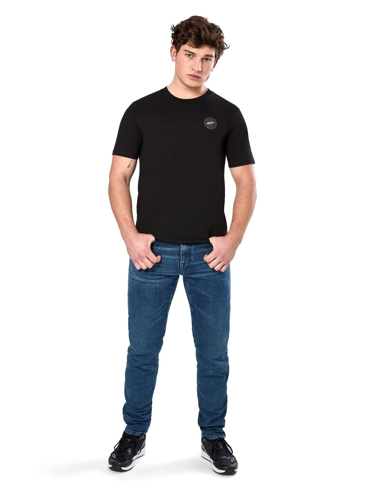 Alpinestars Dot Carbon CSF Tee, camiseta de manga corta, negra, pequeño logo circular Astars Dot en el pecho, combinada con vaqueros azules y zapatillas negras, ropa urbana casual de motorsport