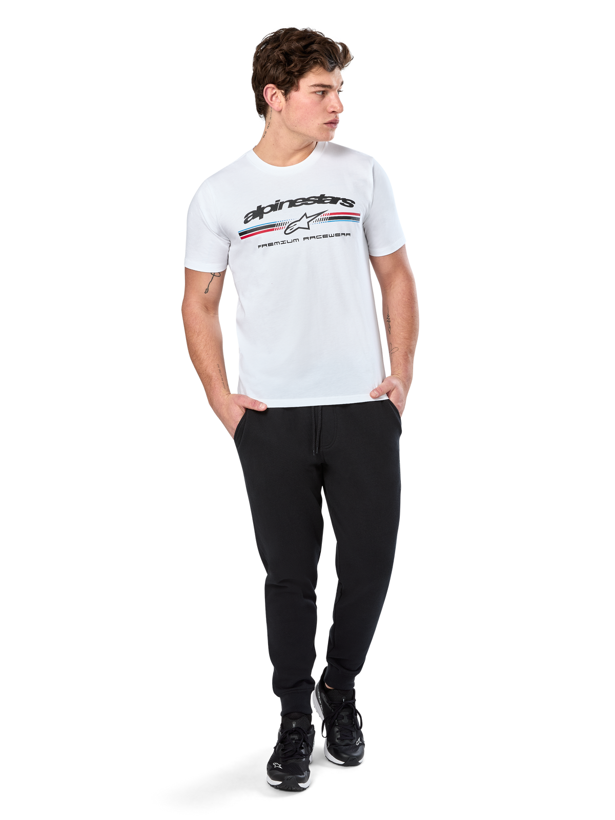 Alpinestars Prevail CSF Tee, Short Sleeve T-Shirt, White, featuring a front paddock-style tri-color stripe logo with Alpinestars branding, worn by a model with black joggers and black sneakers, casual motorsport streetwear