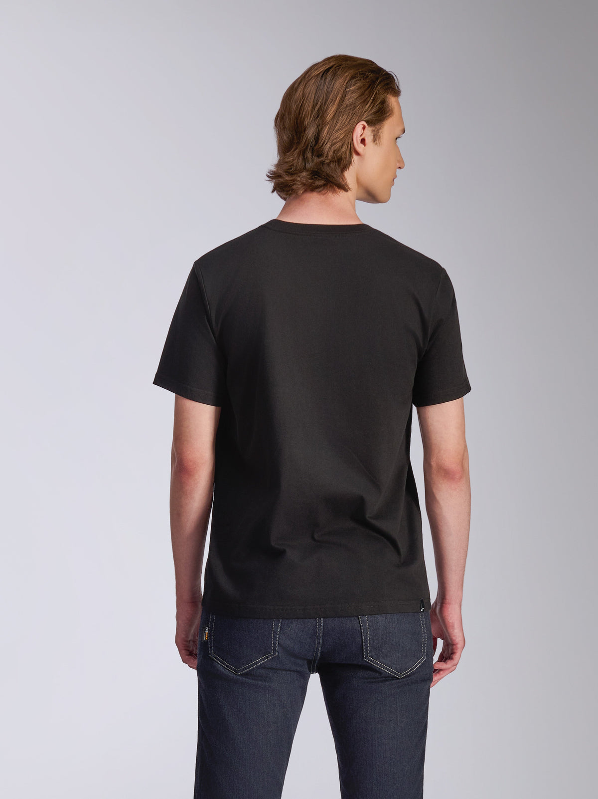 Camiseta Alpinestars Luxo CSF, camiseta de manga corta, negra, vista posterior, usada por un modelo con vaqueros azul oscuro, ropa de calle casual inspirada en el automovilismo