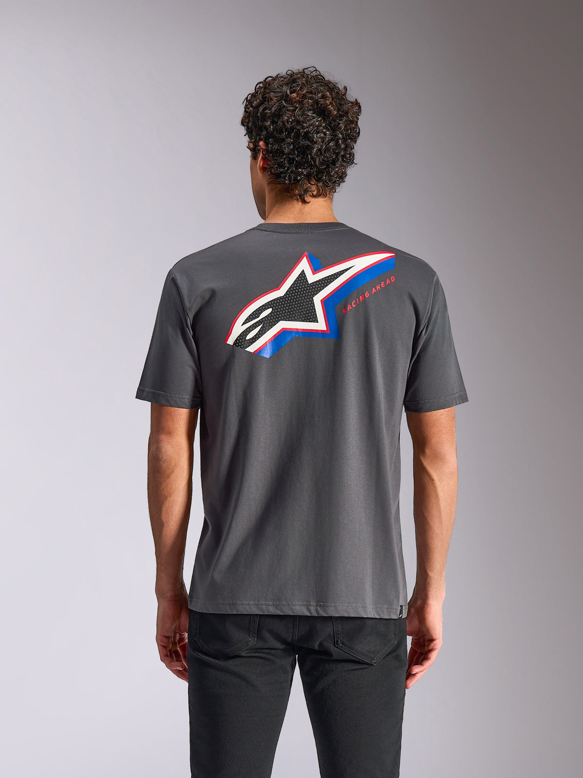 Camiseta Alpinestars Angler CSF de manga corta, gris carbón, vista trasera con un logotipo grande de Astars con detalles en azul y rojo y el texto 'RACING AHEAD', estilo casual de ropa urbana de deportes de motor