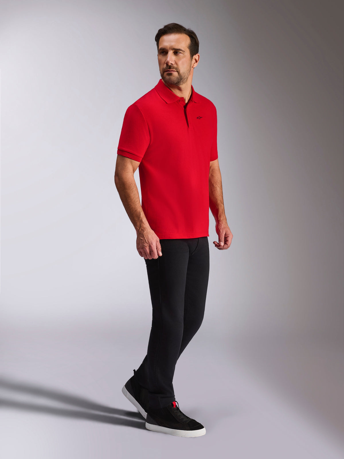 Alpinestars Endeavor Classic Polo, polo de piqué de manga corta rojo, pequeño logo negro de Astars, cuello y puños acanalados, usado por un modelo con pantalones negros y zapatillas, estilo casual inspirado en el automovilismo