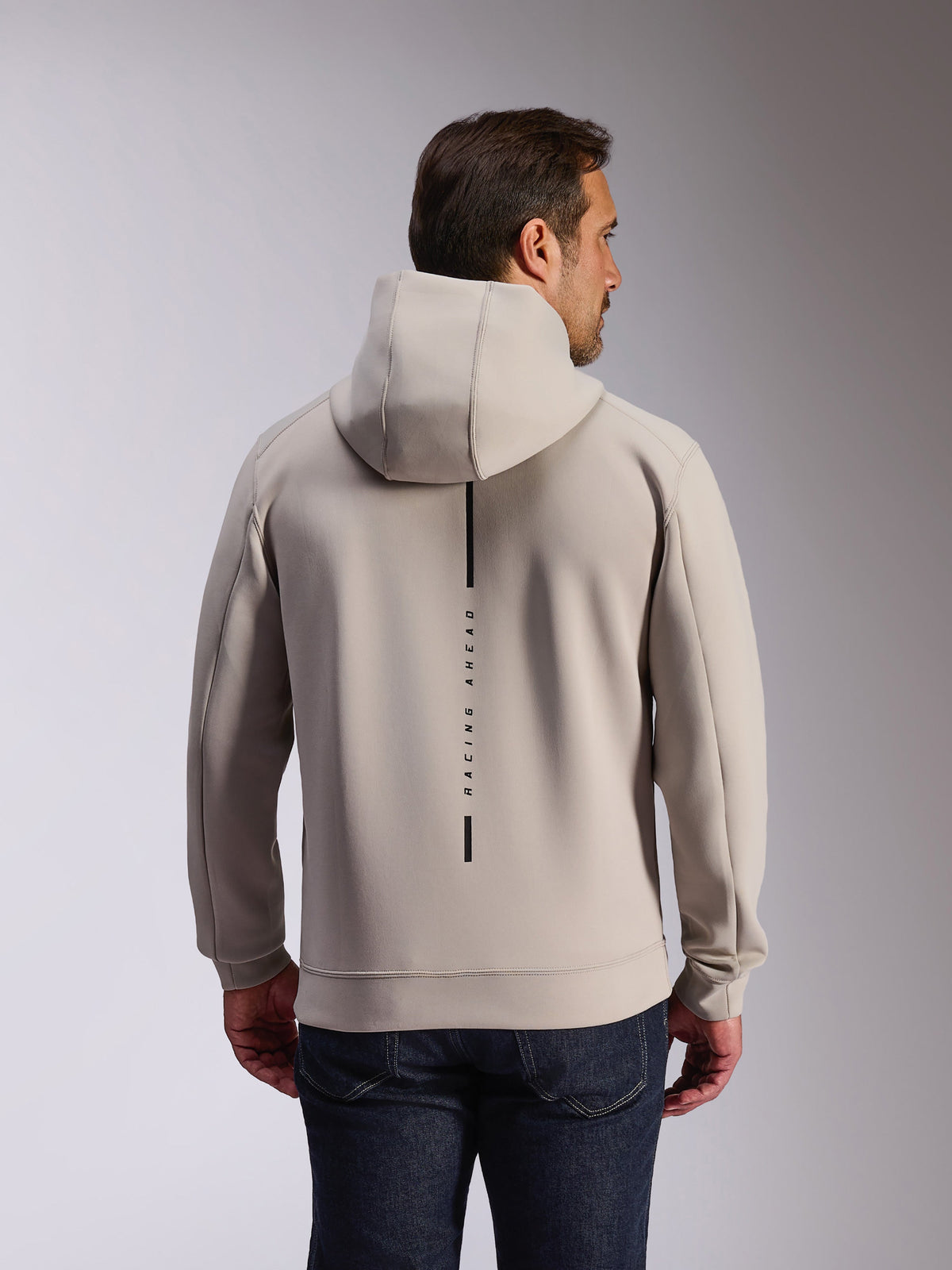 Alpinestars Insight Hoodie en color Cement, vista posterior de un modelo con sudadera gris claro, cuenta con un logo de franja vertical negra con el texto 'RACING AHEAD', sudadera casual de forro polar de doble cara de inspiración deportiva
