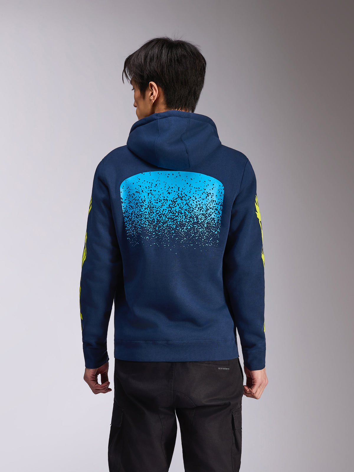 Alpinestars Obsessed Hoodie, sudadera con capucha de forro polar azul marino, vista posterior con un gran gráfico de degradado MX en azul claro, logotipo de Alpinestars en amarillo en las mangas, ropa urbana casual de inspiración motorsport