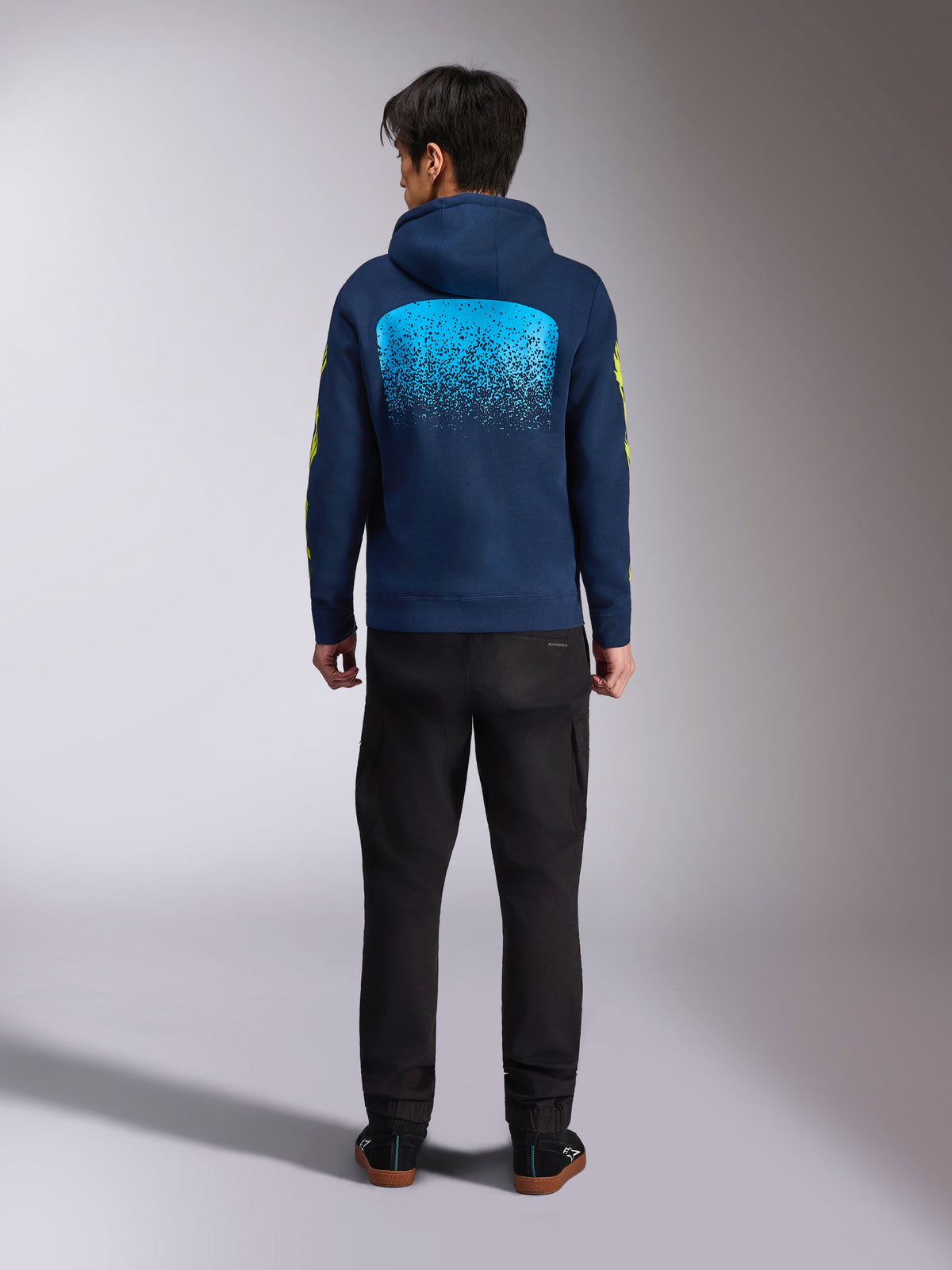 Sudadera con capucha Alpinestars Obsessed en azul marino, vista posterior con un gran gráfico de degradado MX en cian y logotipos amarillos en las mangas, forro polar casual inspirado en el automovilismo.