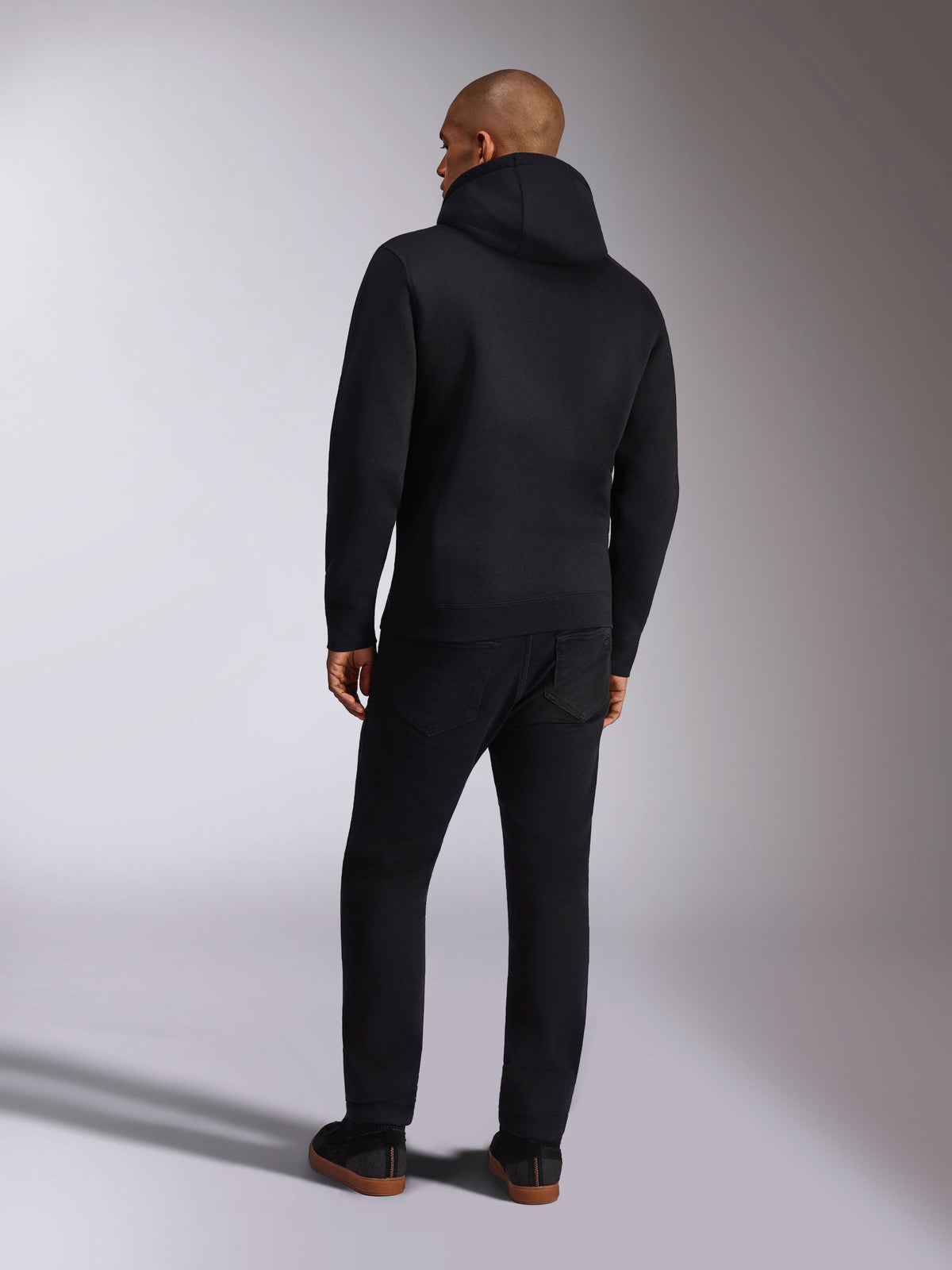 Alpinestars Ellipsoid Hoodie, ropa deportiva casual, sudadera con capucha en color negro sólido, vista trasera, con mangas largas y dobladillo de canalé, combinada con pantalones negros, diseño moderno inspirado en el automovilismo
