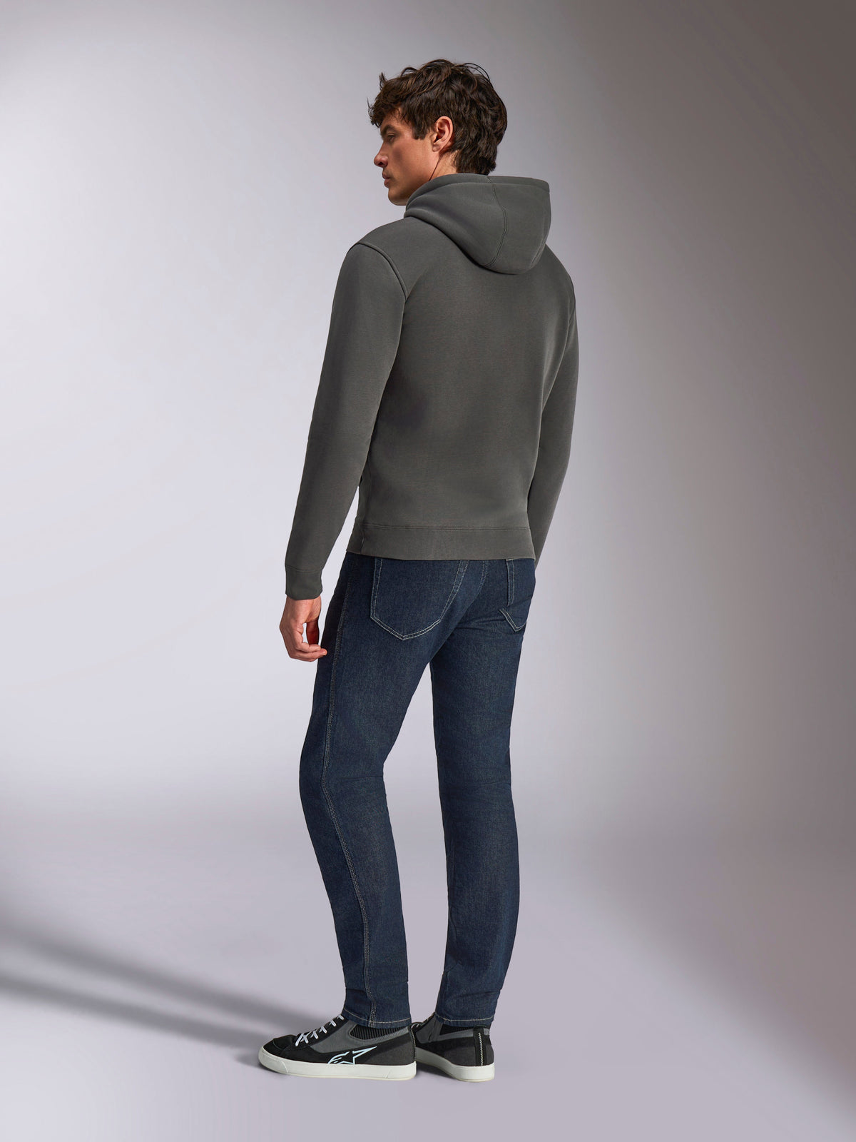 Sudadera con capucha Alpinestars Ellipsoid, ropa deportiva casual, gris plomo, vista trasera en modelo masculino, capucha con cordón, manga larga, puños y dobladillo de canalé, combinada con vaqueros oscuros y zapatillas