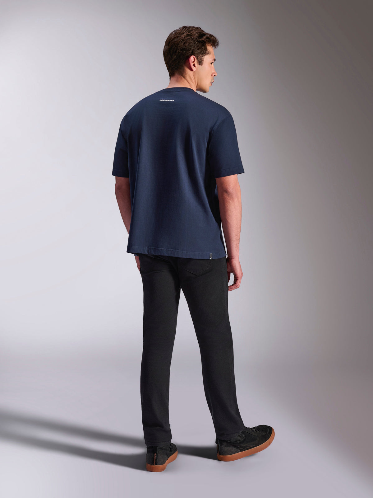 Alpinestars Focused Oversized CSF Tee, camiseta de manga corta, azul marino, vista posterior con pequeño logotipo de Alpinestars en blanco en el cuello, combinada con pantalones negros, ropa casual de estilo de vida