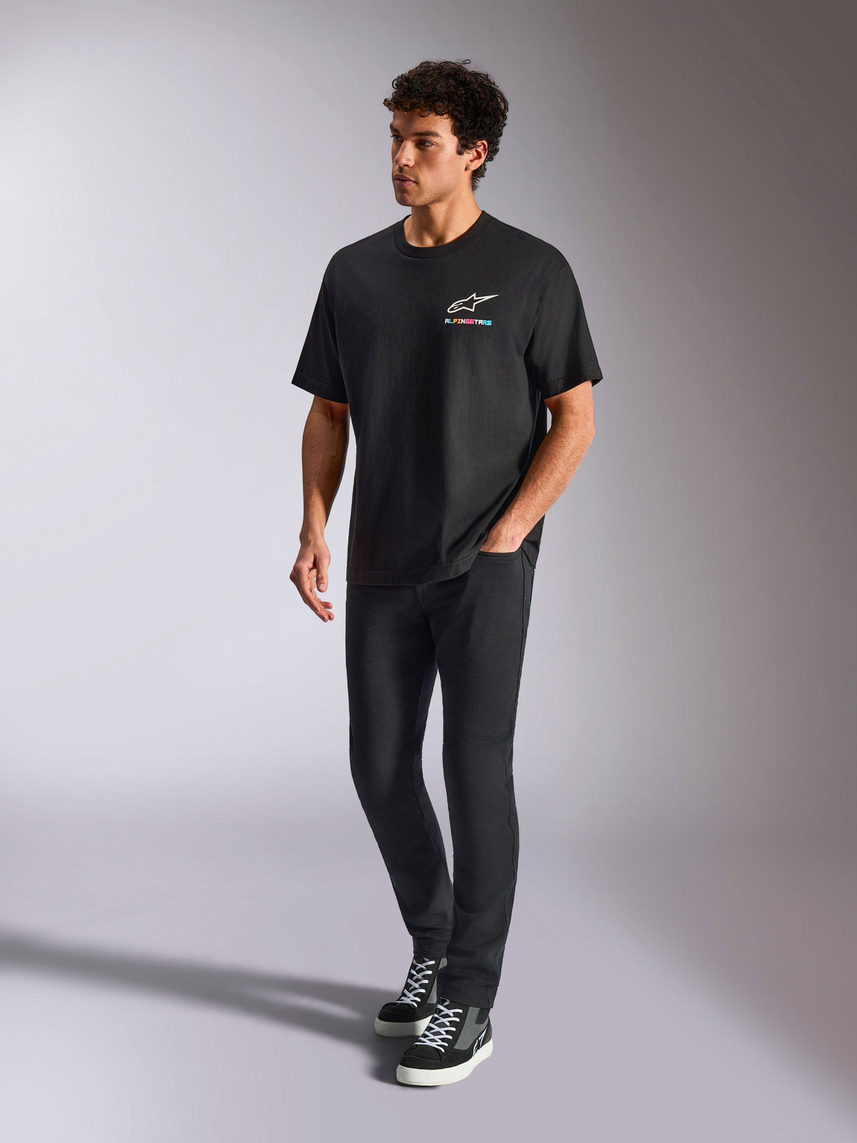 Camiseta Alpinestars Wild Oversized CSF, camiseta de manga corta, negra, logotipo Astars multicolor en el pecho, estilo casual de ropa urbana usado por un modelo con pantalones negros y zapatillas de caña alta