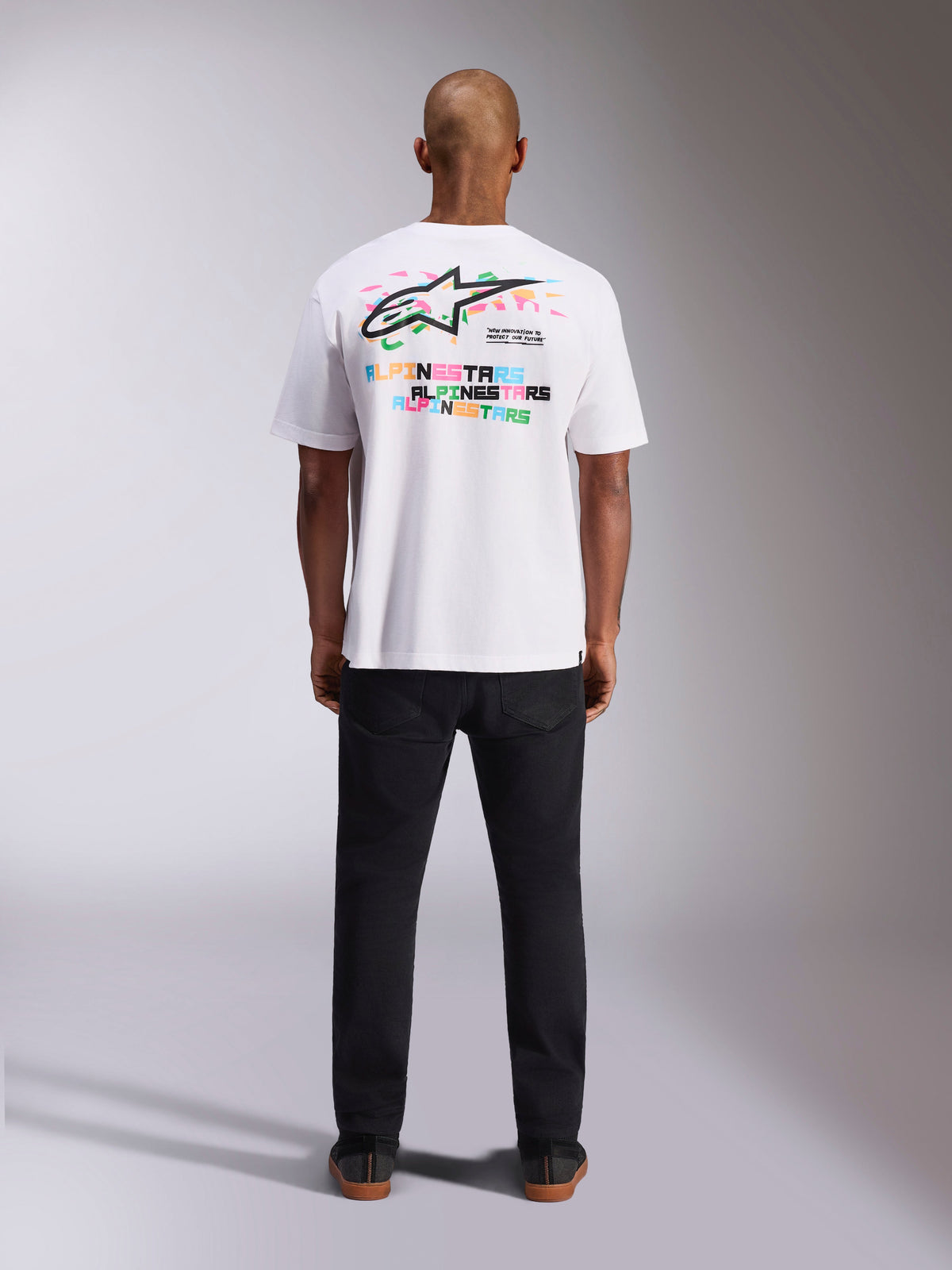 Alpinestars Wild Oversized CSF Tee, camiseta de manga corta, blanca, vista posterior que muestra un vibrante logo Astars multicolor y tipografía repetida, ropa urbana casual de inspiración motorsport