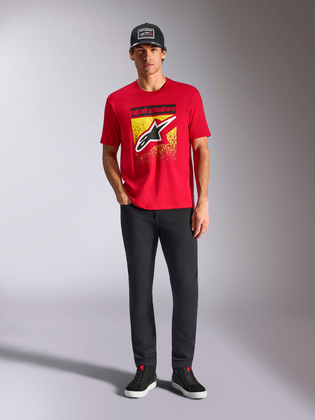 Alpinestars Noka CSF Tee, Short Sleeve T-Shirt, Red, featuring a large front Astars logo with yellow and black MX gradation, worn with black pants and a black cap, Casual Motorsport Streetwear