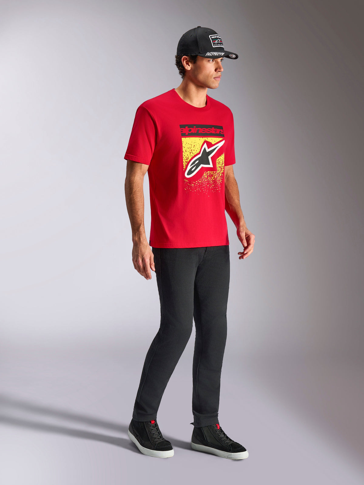 Alpinestars Noka CSF Tee, Short Sleeve T-Shirt, Red, featuring front Astars logo with MX gradation on a yellow graphic, worn with a black Alpinestars cap and black pants, casual motorsport streetwear