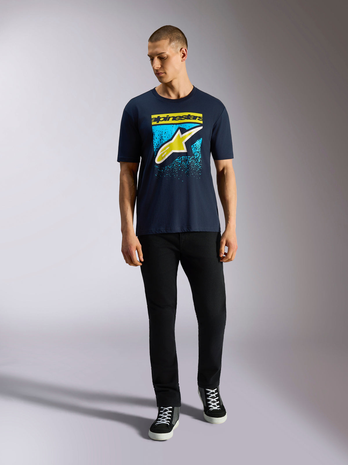 Camiseta Alpinestars Noka CSF, camiseta de manga corta, azul marino, logo Astars frontal con degradado MX en amarillo y azul claro, usada por un modelo con pantalones negros, ropa urbana casual de automovilismo