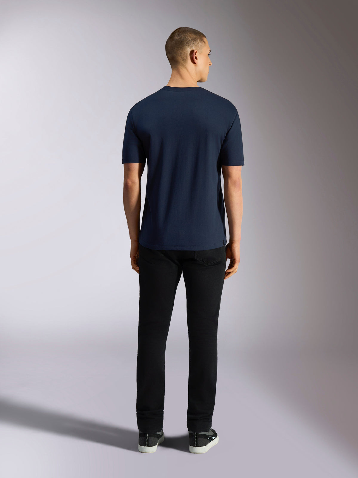 Alpinestars Noka CSF Tee, camiseta de manga corta, azul marino, vista posterior de un hombre llevando la camiseta combinada con pantalones negros y zapatillas, estilo casual motorsport streetwear