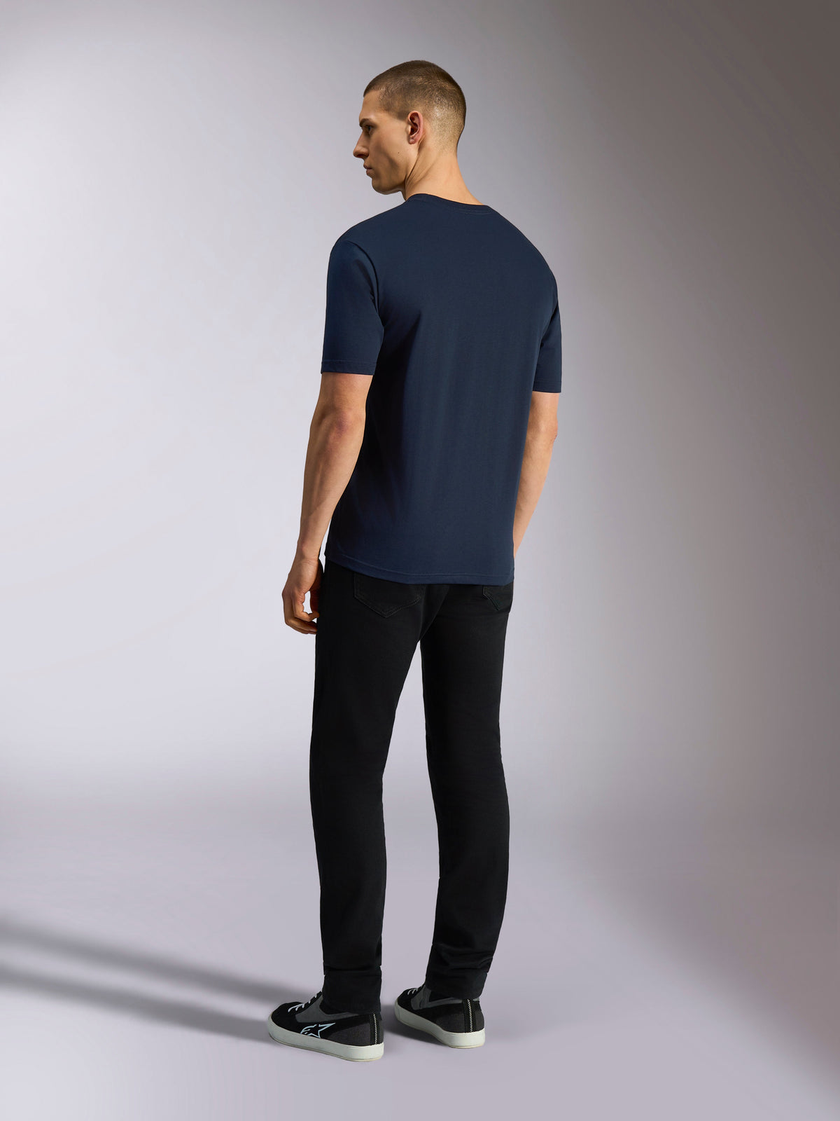 Camiseta Alpinestars Noka CSF, camiseta de manga corta, azul marino, vista posterior mostrada en un modelo que viste pantalones negros y zapatillas, ropa urbana casual de motorsport