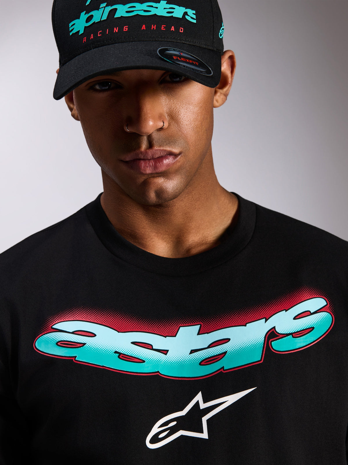 Camiseta Alpinestars Ellipsoid CSF, camiseta de manga corta, negra, palabra Astars con degradado en verde azulado y blanco y detalles de semitono rojos, logo Astars blanco, usada con gorra Alpinestars negra a juego, ropa urbana casual de automovilismo