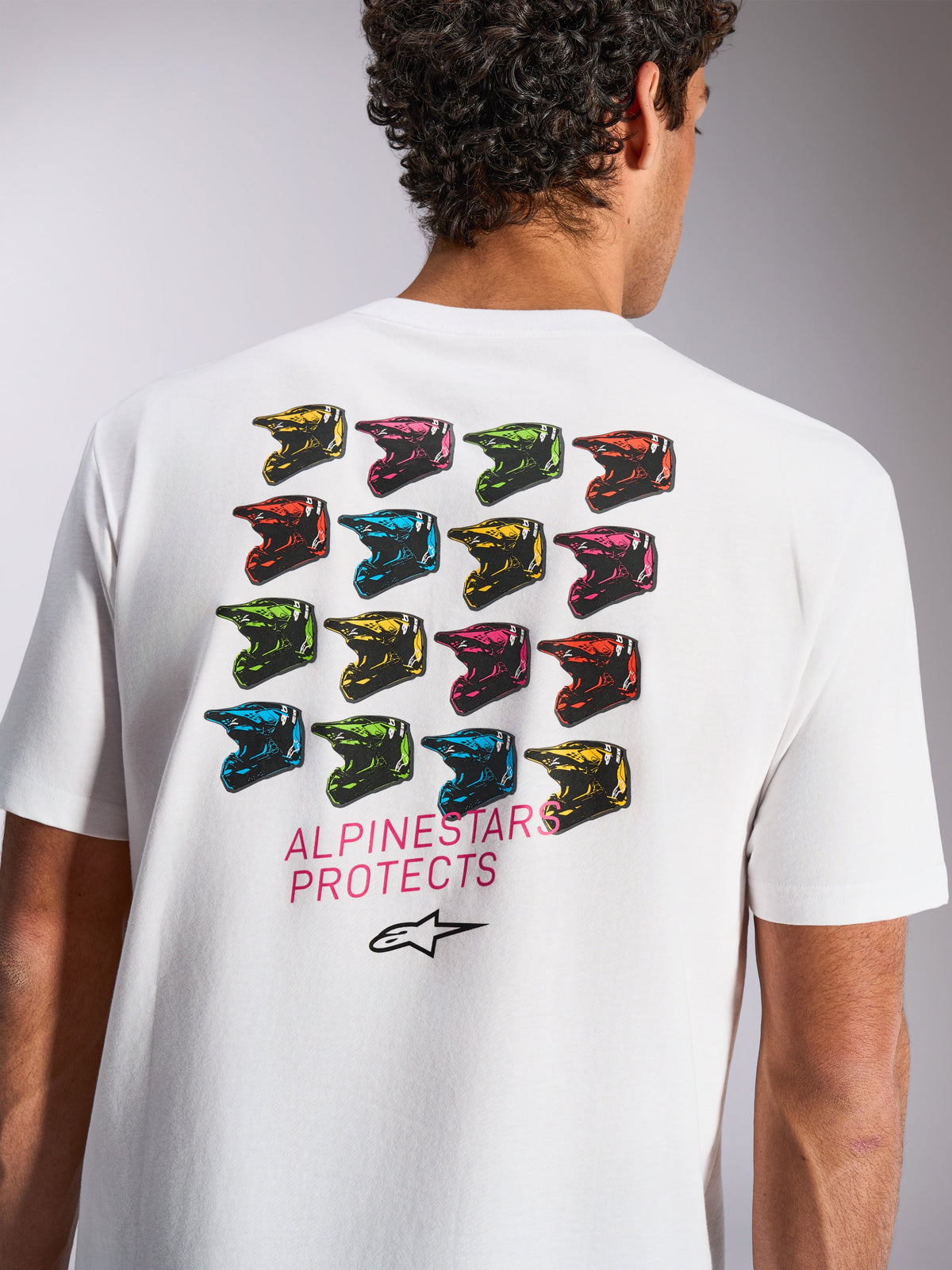 Camiseta Alpinestars Pop Helmet CSF, camiseta de manga corta, blanca, gráfico en la espalda con una cuadrícula de coloridos cascos M10, texto 'ALPINESTARS PROTECTS' y logotipo de Astars, ropa deportiva casual de motor