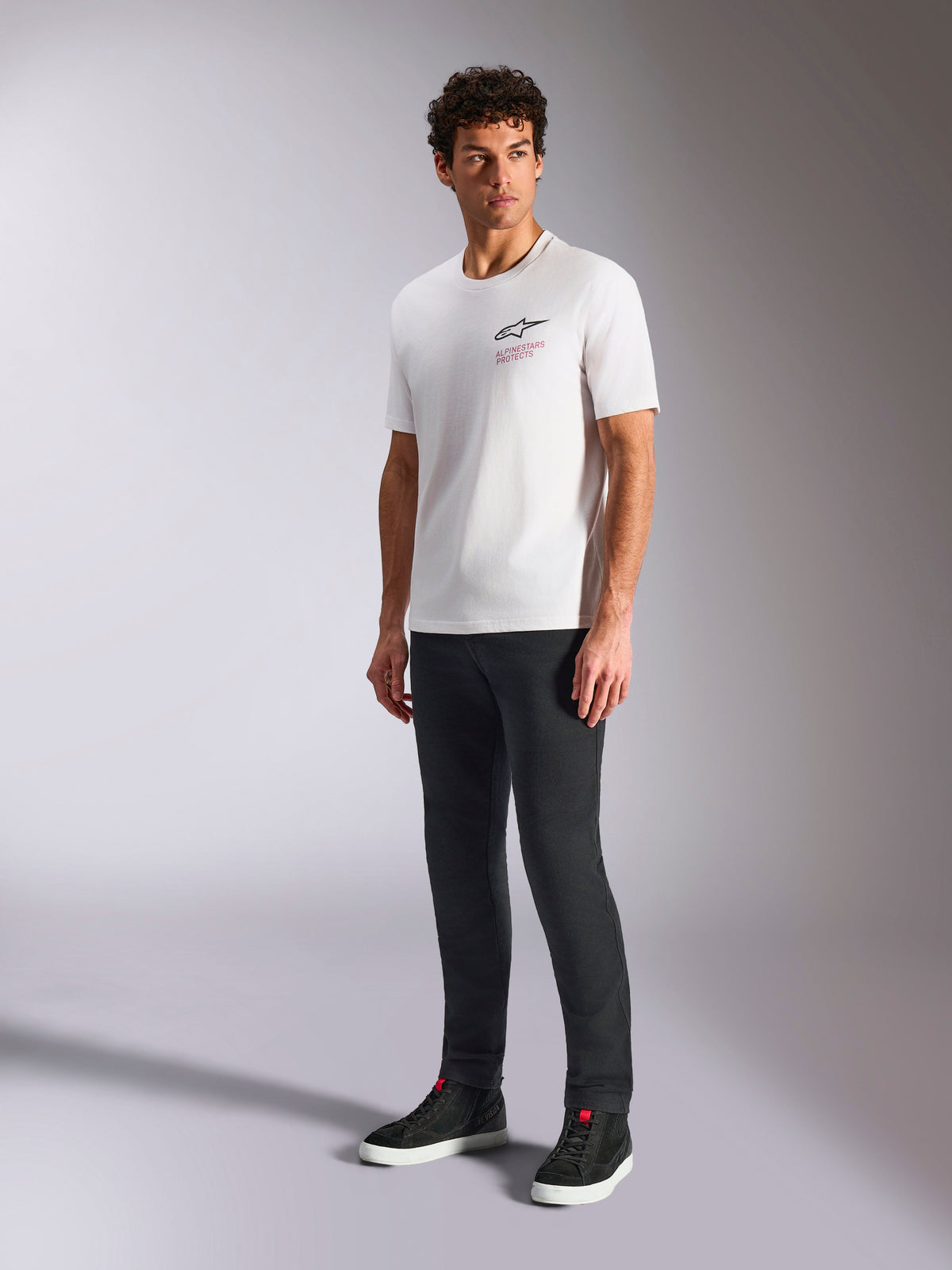 Alpinestars Pop Helmet CSF Tee, camiseta de manga corta blanca con el logotipo frontal de Astars y texto en rojo, llevada por un modelo masculino con pantalones oscuros y zapatillas negras, ropa urbana casual de estilo motorsport