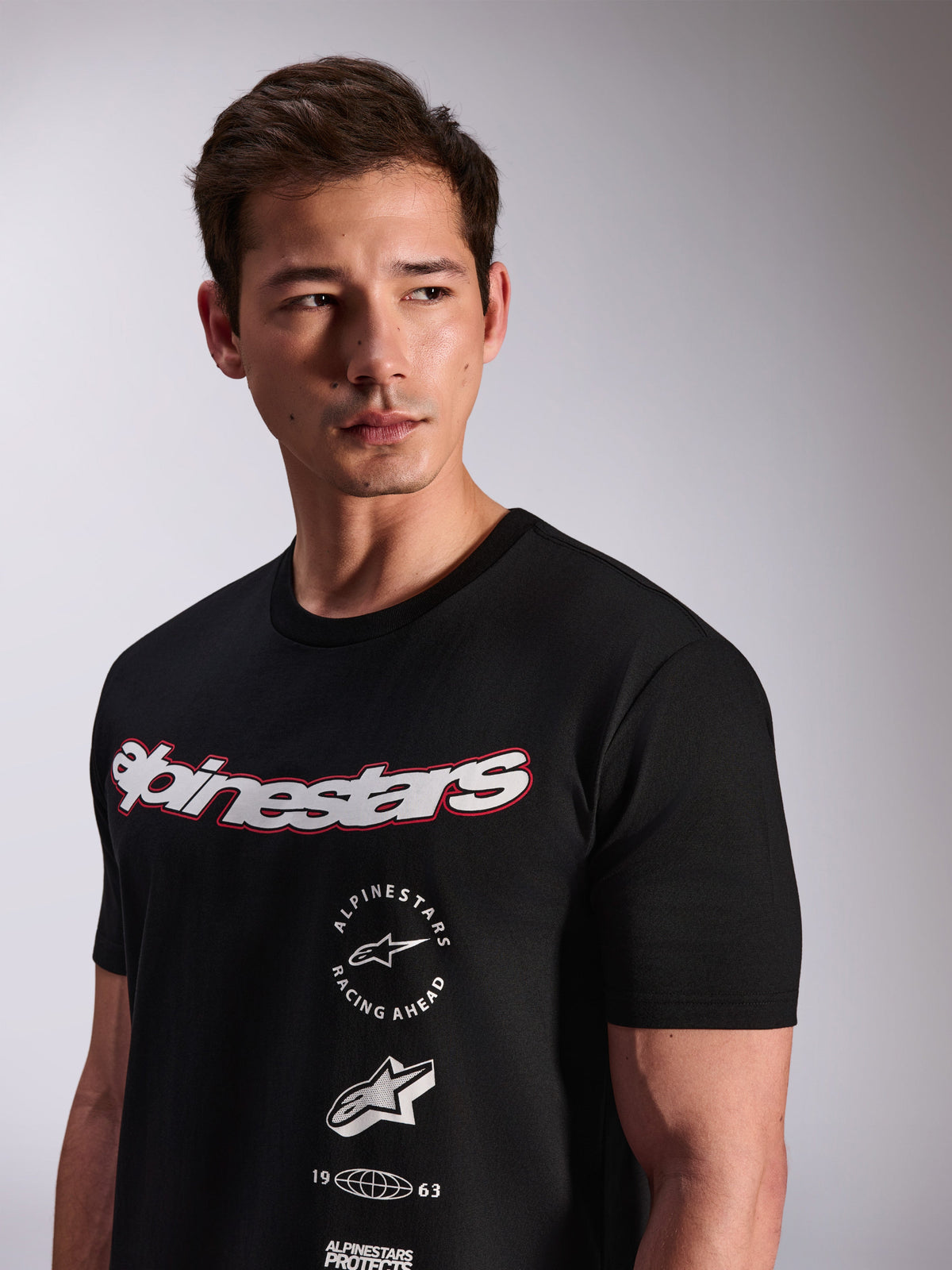 Alpinestars Abus CSF Tee, Short Sleeve T-Shirt, Black, worn by a model, featuring a white Alpinestars script logo with red outline and multi-stacked graphic logos on the chest, Casual Motorsport Streetwear