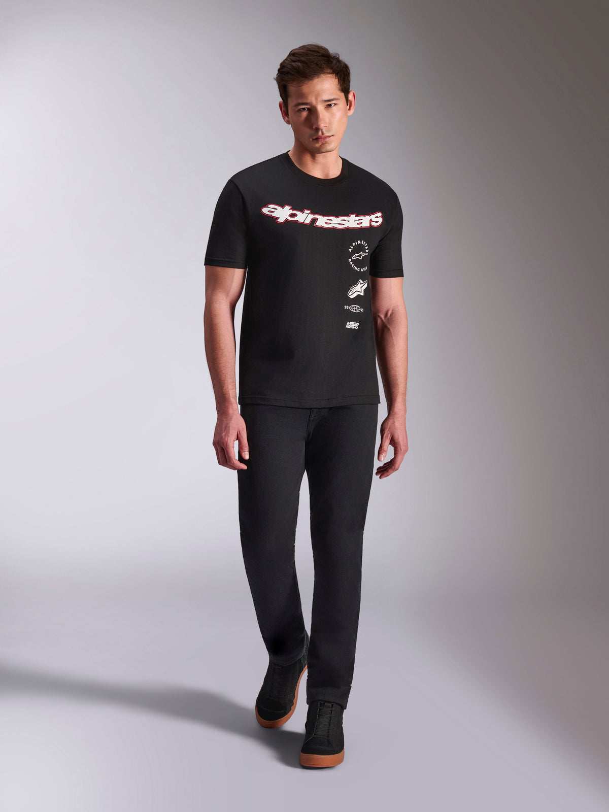 Alpinestars Abus CSF Tee, Short Sleeve T-Shirt, Black, Curved red and white wordmark with multi-stacked logos, worn by male model with black pants and black sneakers, casual motorsport streetwear