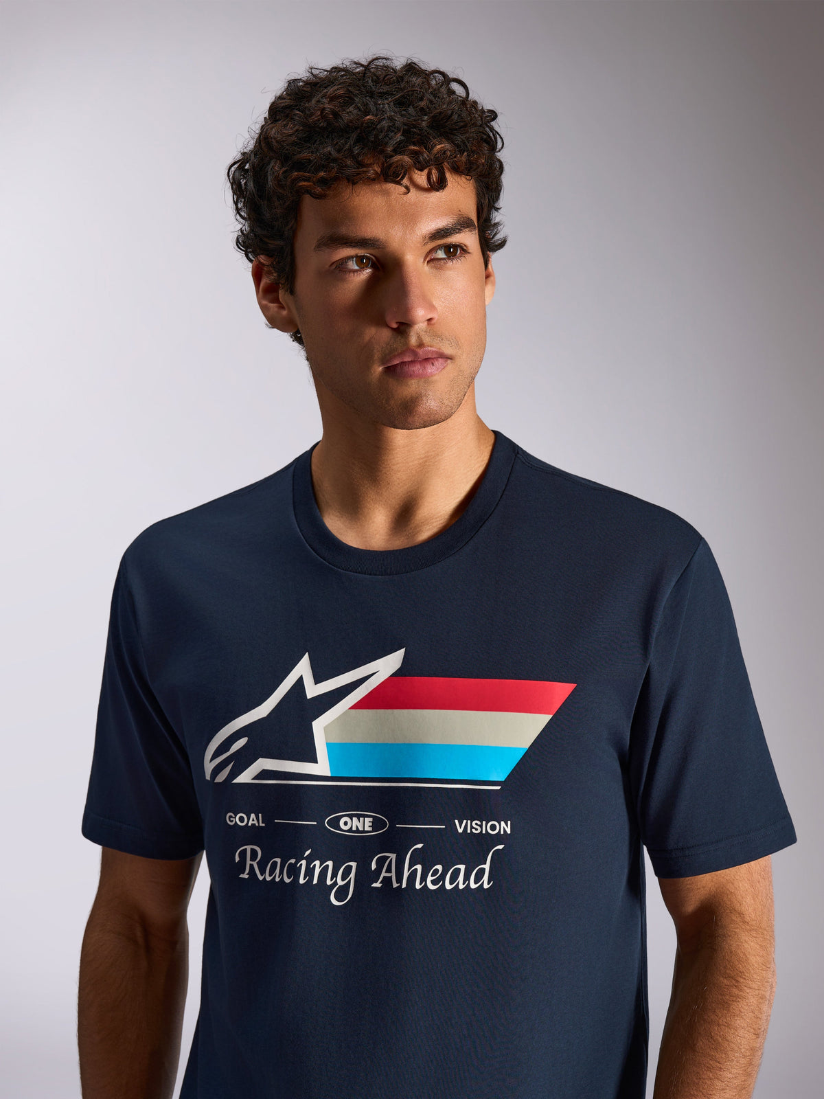 Alpinestars Trifecta CSF Tee, camiseta de manga corta en azul marino, logotipo de Astars blanco con franjas tricolores y texto 'Racing Ahead', imagen de estilo de vida casual de deportes de motor