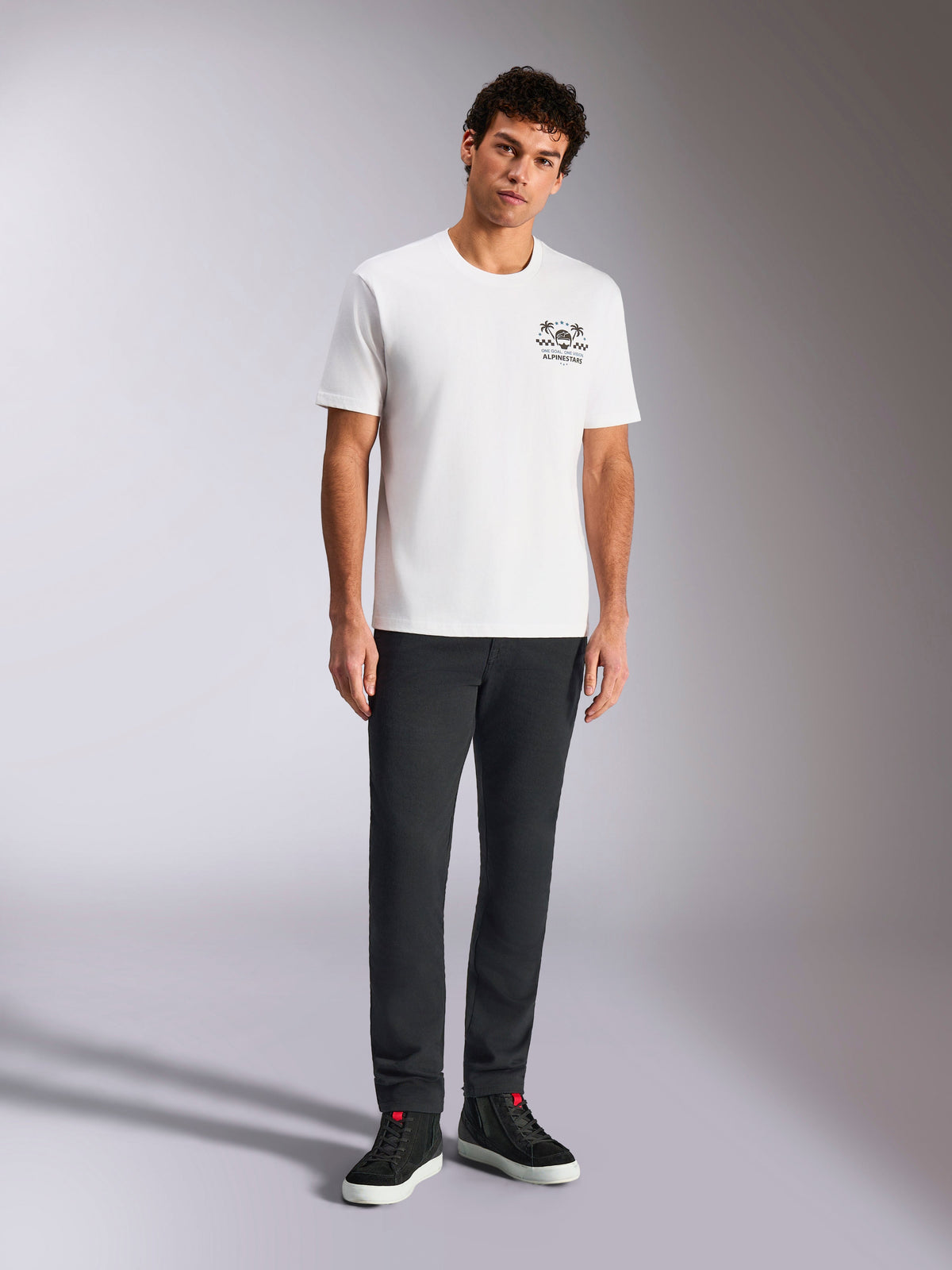 Alpinestars Order CSF Tee, camiseta de manga corta, blanca, pequeño gráfico negro en el pecho con casco y palmeras, ropa urbana de estilo casual motorsport, usada por un modelo con pantalones negros y zapatillas