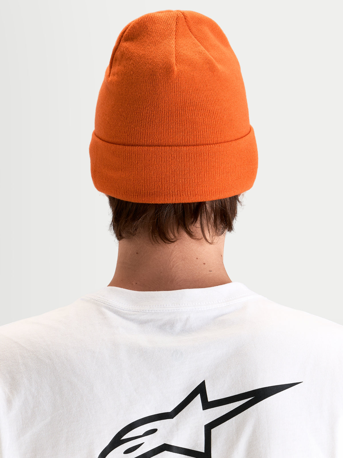 Alpinestars Gorro Augment Cuff, gorro de punto naranja con diseño de vuelta y silueta de ajuste profundo, vista trasera en modelo que lleva una camiseta blanca con el logo Astar negro