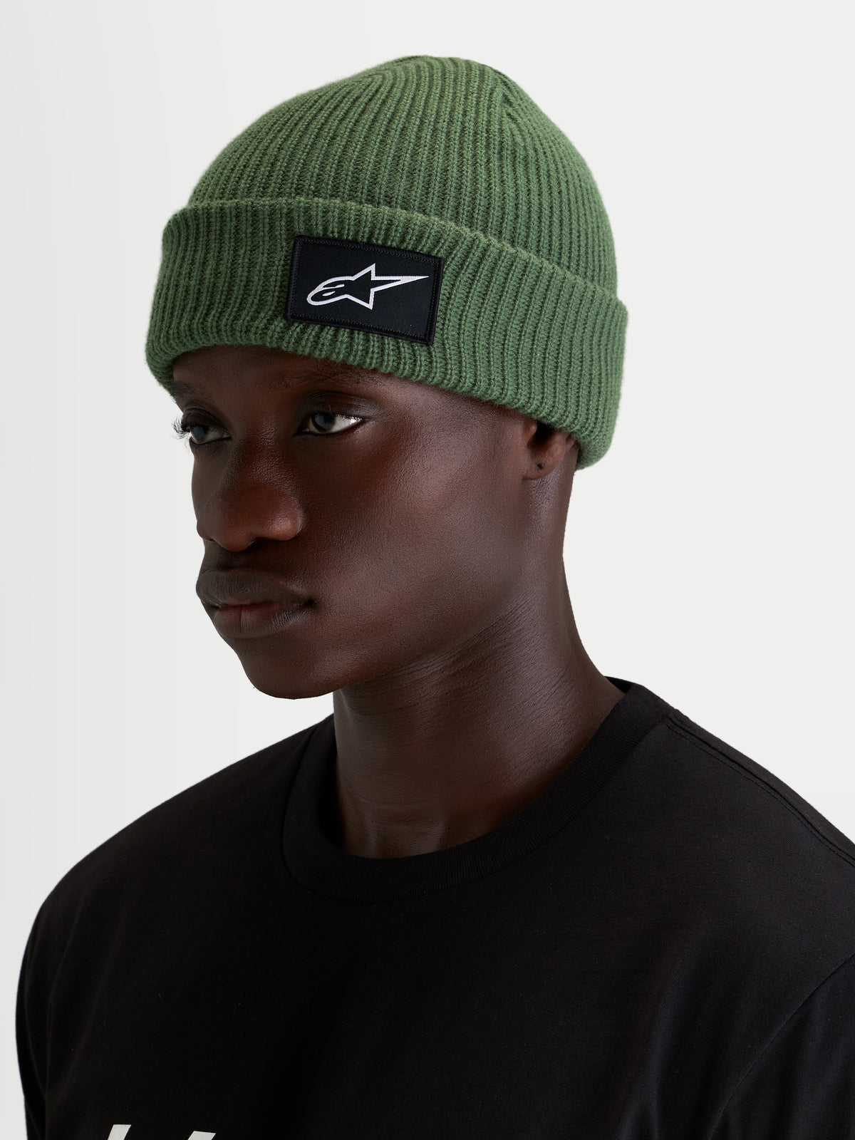 Gorro Unload Rib Cuff Alpinestars, gorro informal de invierno para hombre, verde guisante con construcción de punto jersey y parche frontal tejido, vista en modelo