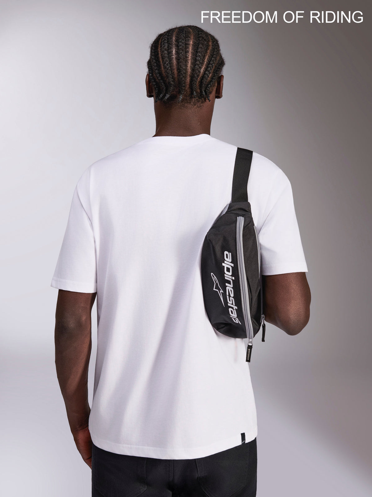 Alpinestars Riñonera Only Linear, riñonera de estilo deportivo urbano, negra y blanca, capacidad de 2 litros, poliéster duradero con logotipo de la marca, mostrada como bolso bandolera cruzado sobre un modelo para uso diario.