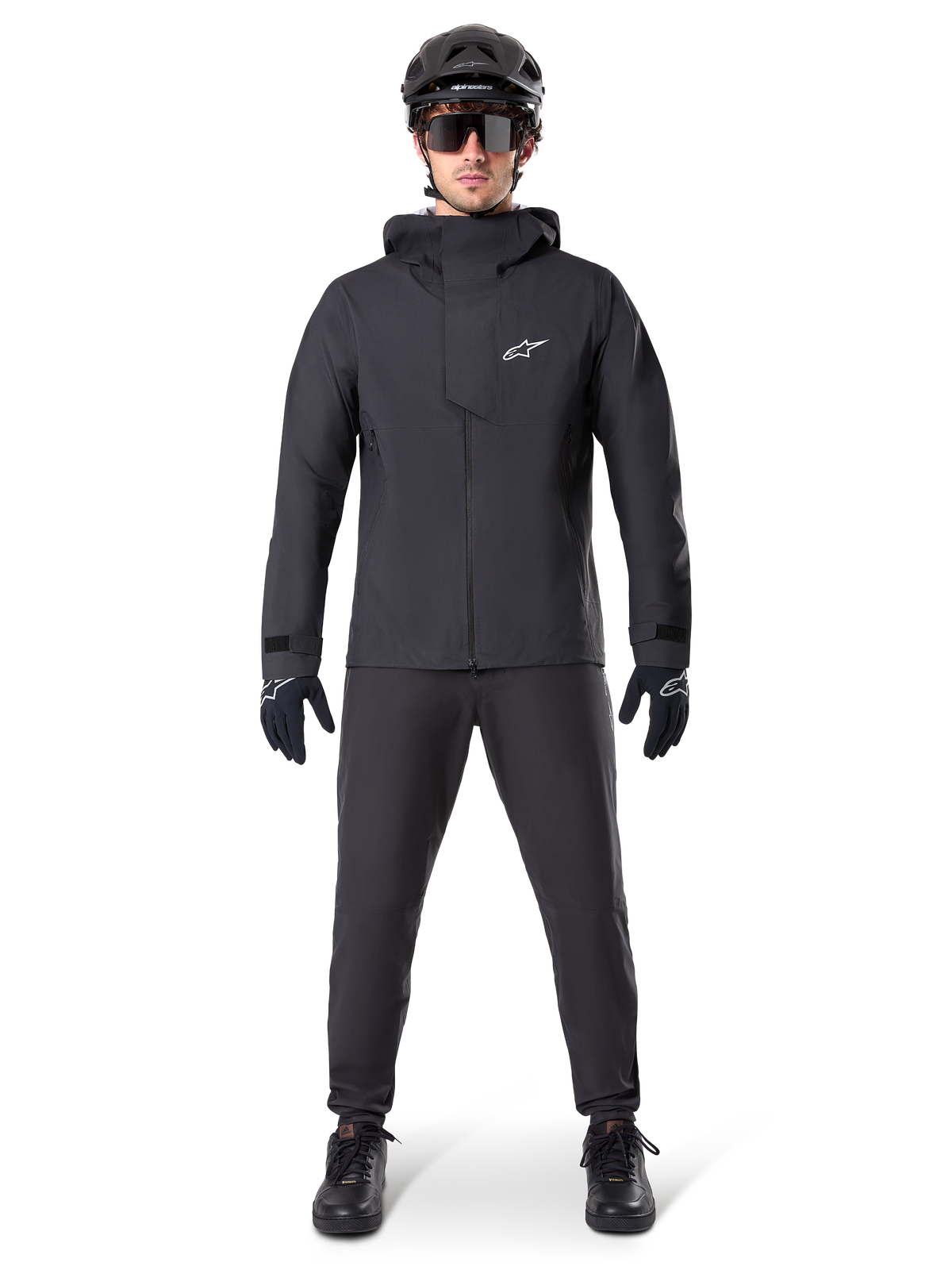 Chaqueta impermeable Alpinestars A-Dura Elite, negra, combinada con pantalones y guantes de ciclismo a juego, casco negro y gafas de sol, con el logotipo de Astars en blanco en el pecho, diseño técnico de alto rendimiento para ciclismo de montaña