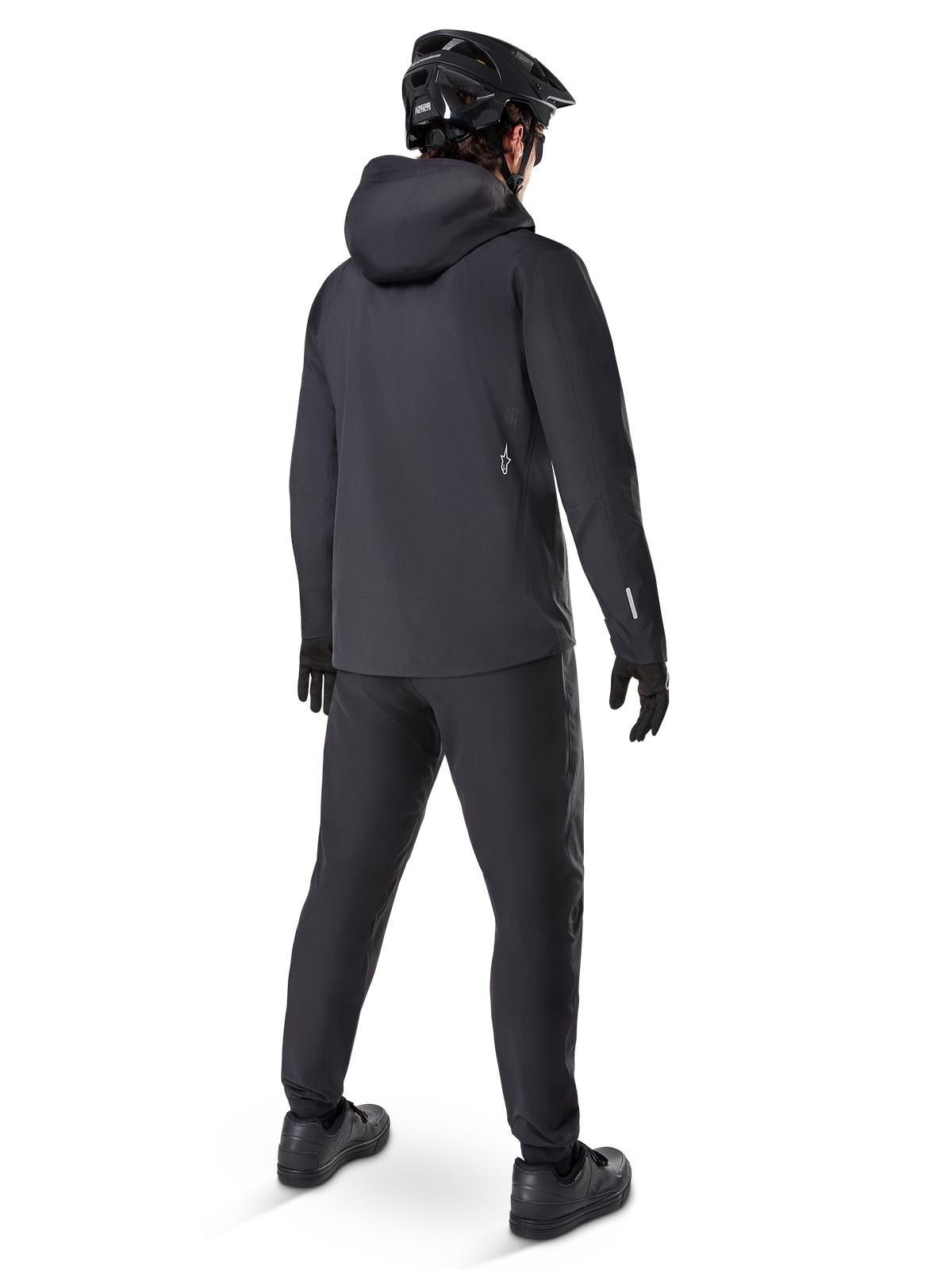 Chaqueta Impermeable Alpinestars A-Dura Elite, color negro, vista trasera que muestra la capucha compatible con el casco y el dobladillo trasero más largo, combinada con pantalones de MTB, guantes y casco negros a juego para una protección completa en senderos bajo cualquier condición climática.