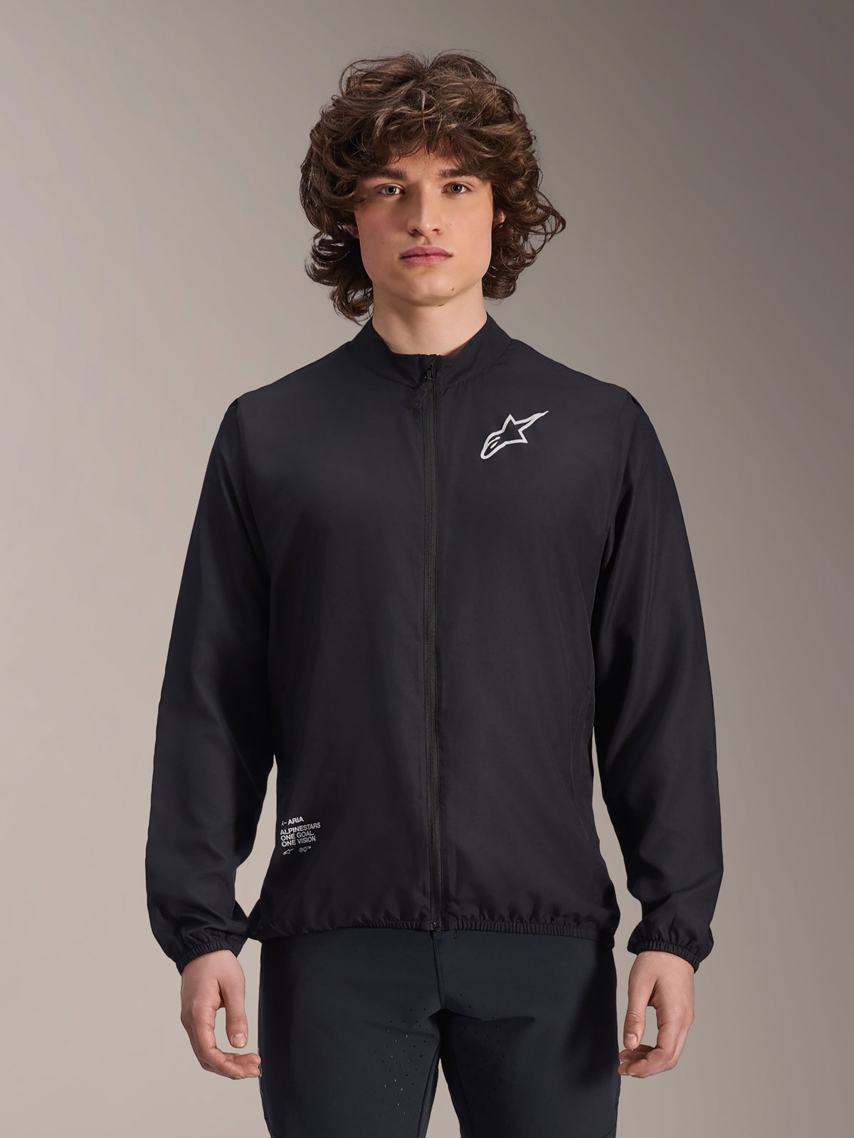 Chaqueta cortavientos Alpinestars A-Aria, negra, chaqueta de ciclismo ligera, con el logotipo Astars blanco en el pecho y detalles de marca en la parte inferior derecha, cremallera frontal completa, cuello alto, puños y dobladillo elásticos, ajuste de rendimiento para deportes al aire libre