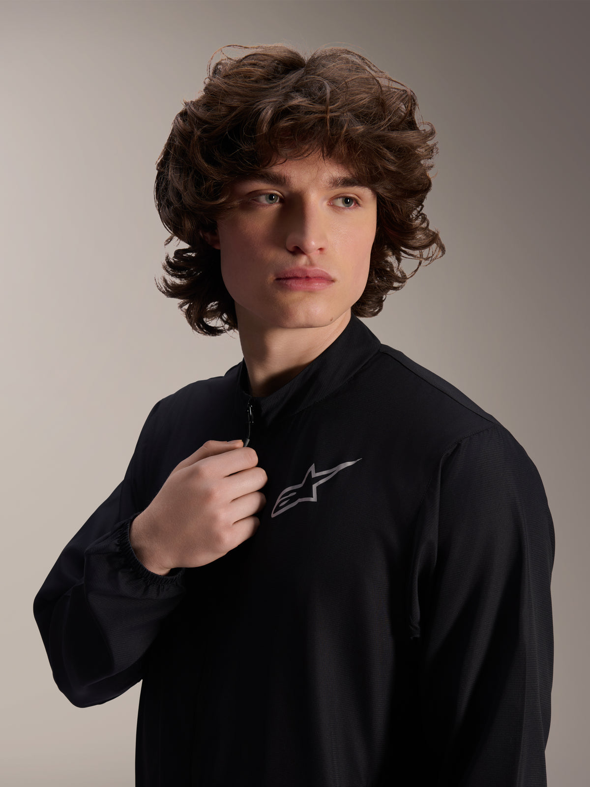 Alpinestars A-Aria Windbreaker Jacket, chaqueta de ciclismo negra, usada por un modelo masculino, diseño de cuello simulado con un logotipo Astars plateado en el pecho, equipamiento de MTB de alto rendimiento ligero y resistente al viento
