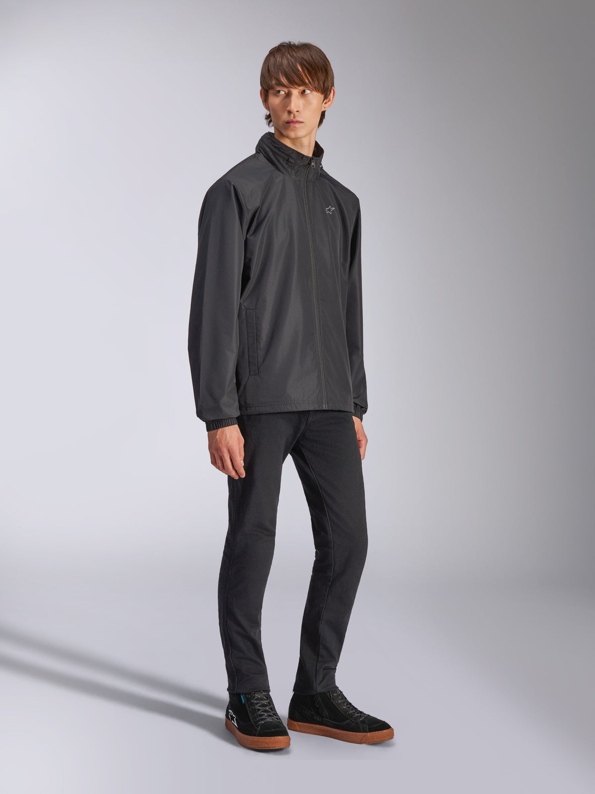 Chaqueta Alpinestars Overhaul Racer, chaqueta impermeable negra, usada con pantalones negros y zapatillas negras con suela de goma, con un logotipo de estrella blanca en el pecho, frente con cremallera, ropa deportiva casual de inspiración motorsport