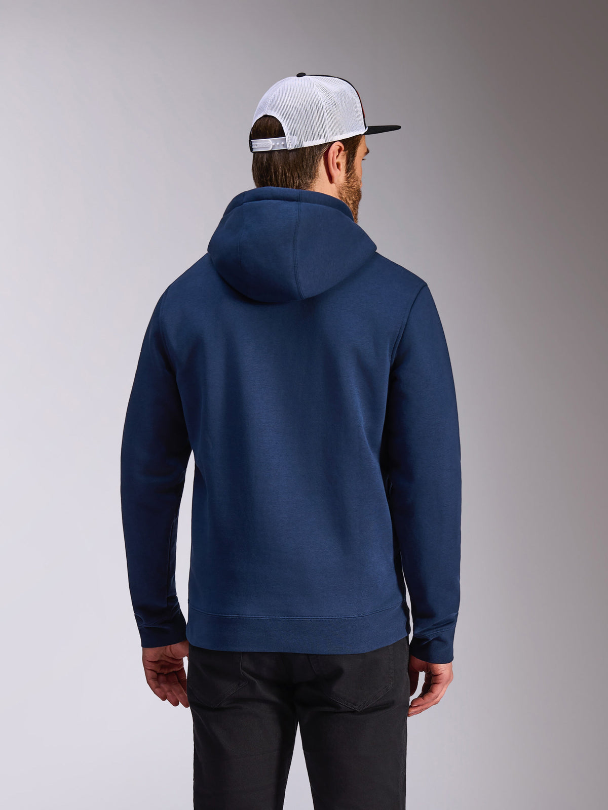 Alpinestars Frontal Hoodie, sudadera de forro polar azul marino, vista trasera de ropa urbana casual, combinada con pantalones negros y una gorra de rejilla blanca y negra, diseño moderno inspirado en el automovilismo