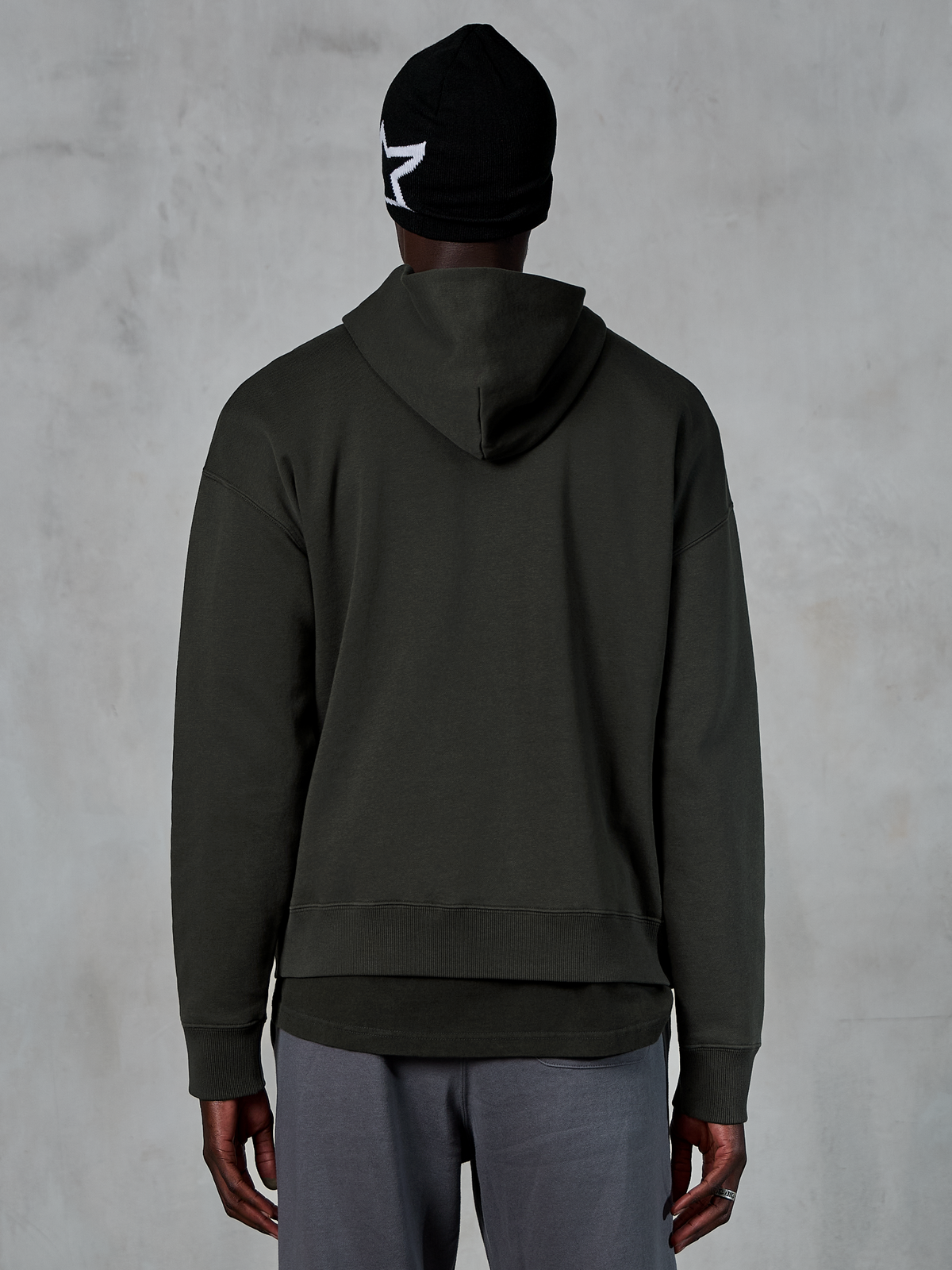 Sudadera con capucha Alpinestars Essentials Ageless, vista trasera, Off Black, ropa urbana casual, modelo con gorro negro con logo de estrella blanca y pantalones grises, forro polar premium con acabado lavado a la piedra