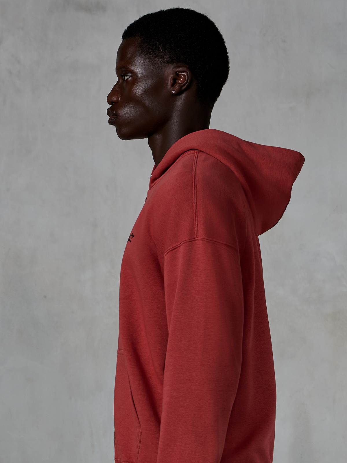 Alpinestars Essentials Ageless Zip Hoodie, sudadera en color rojo ladrillo, vista de perfil lateral de un hombre con sudadera de ajuste relajado y cremallera, pequeño logo de estrella negra en el pecho, forro polar premium con lavado a la piedra, ropa urbana casual inspirada en el motociclismo