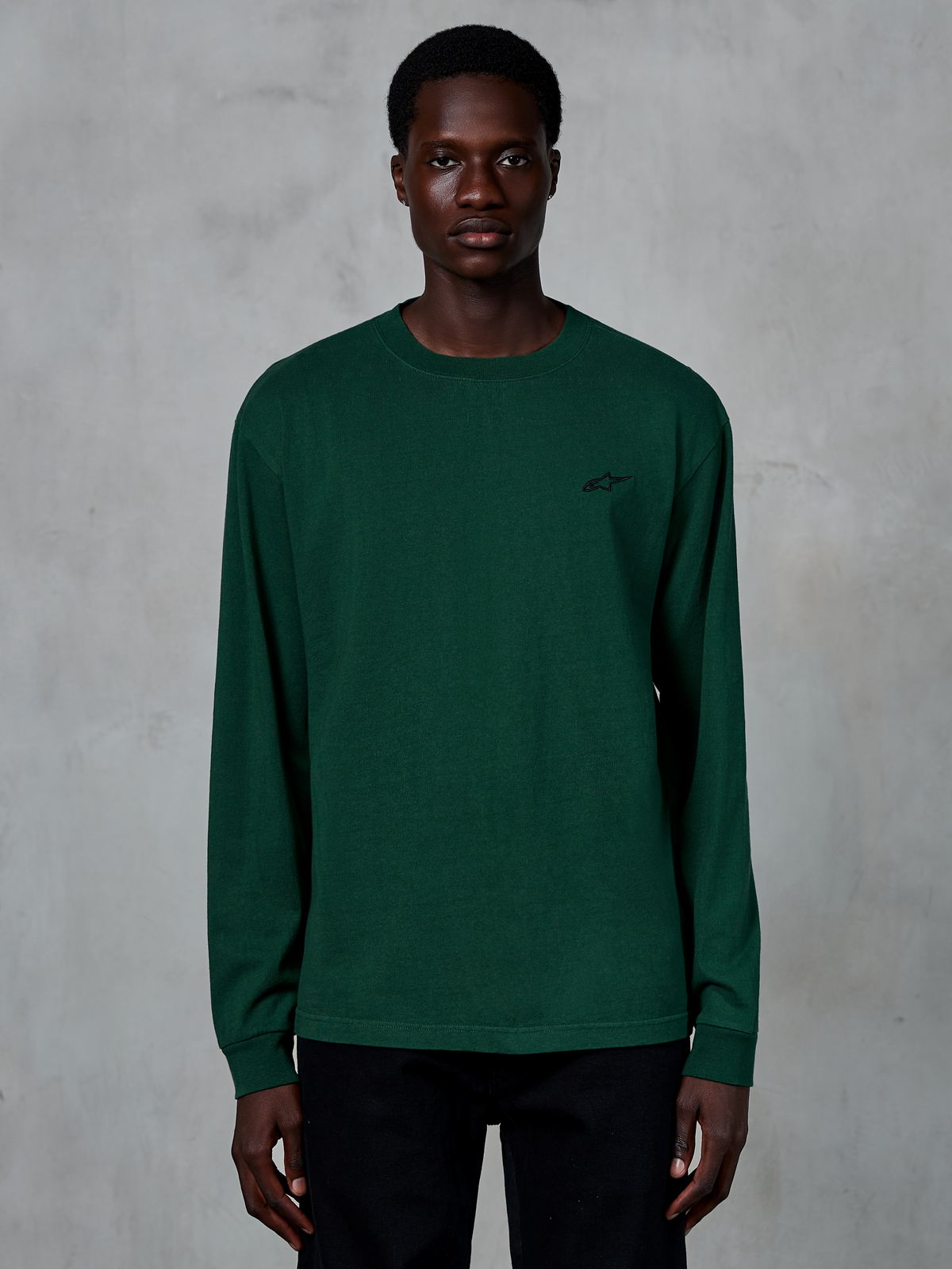 Camiseta de manga larga Alpinestars Essentials Ageless, color verde pino, vista en modelo, pequeño logotipo negro en el pecho, ropa urbana casual, 100% algodón orgánico con acabado de lavado a la piedra