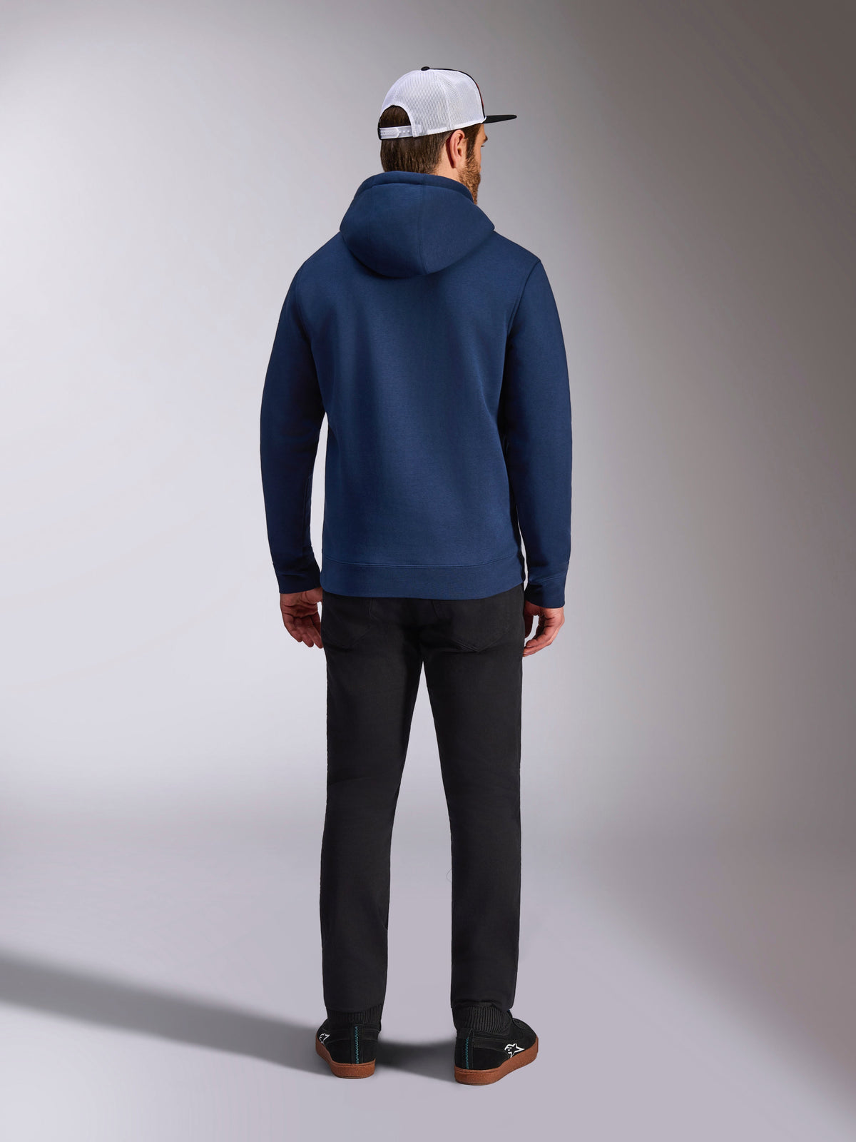 Alpinestars Frontal Hoodie, azul marino, vista trasera de un hombre con sudadera casual de forro polar con capucha, con puños y dobladillo de canalé, combinada con pantalones negros y una gorra de malla blanca, ropa urbana inspirada en el automovilismo